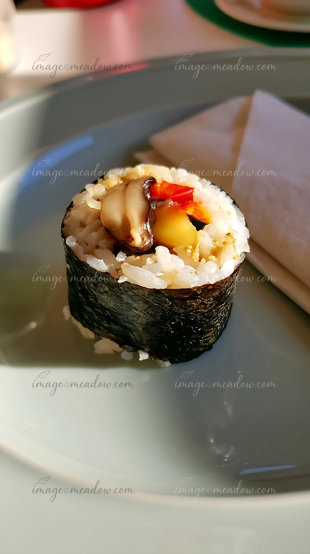 Close-up of a single sushi roll on a contemporary dining table with rice, nori, and colorful filling.