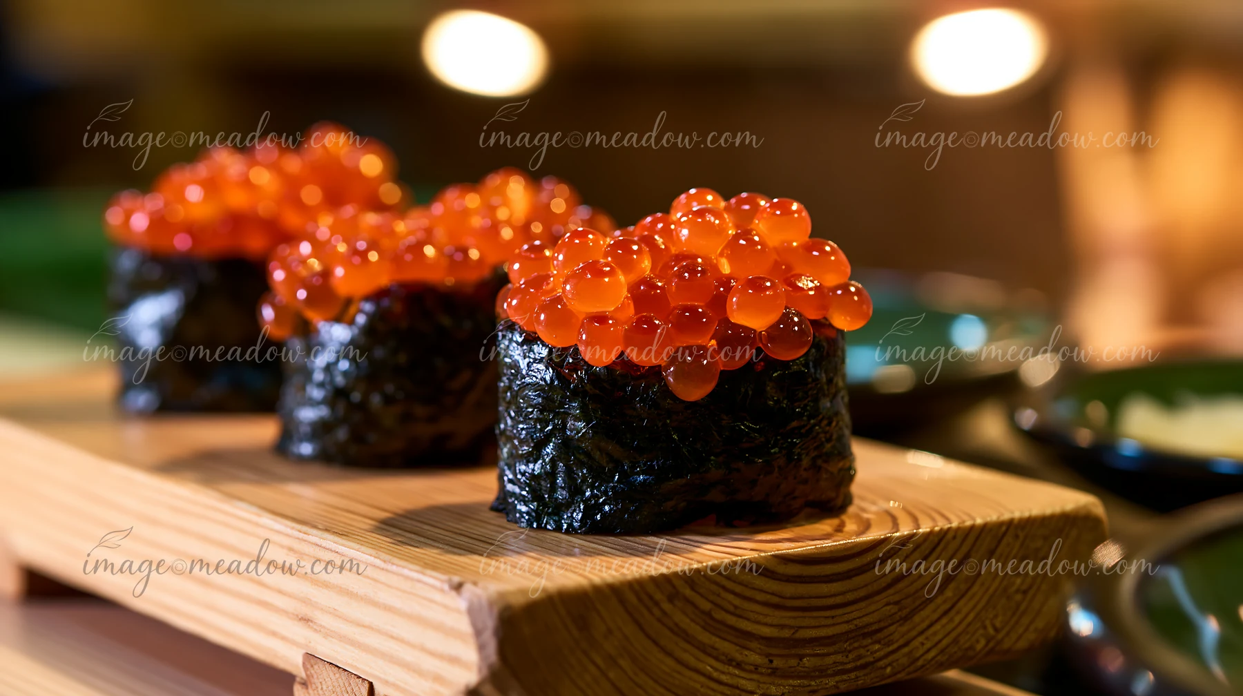 Clusters of ikura salmon roe sushi sit on a wooden platter.
