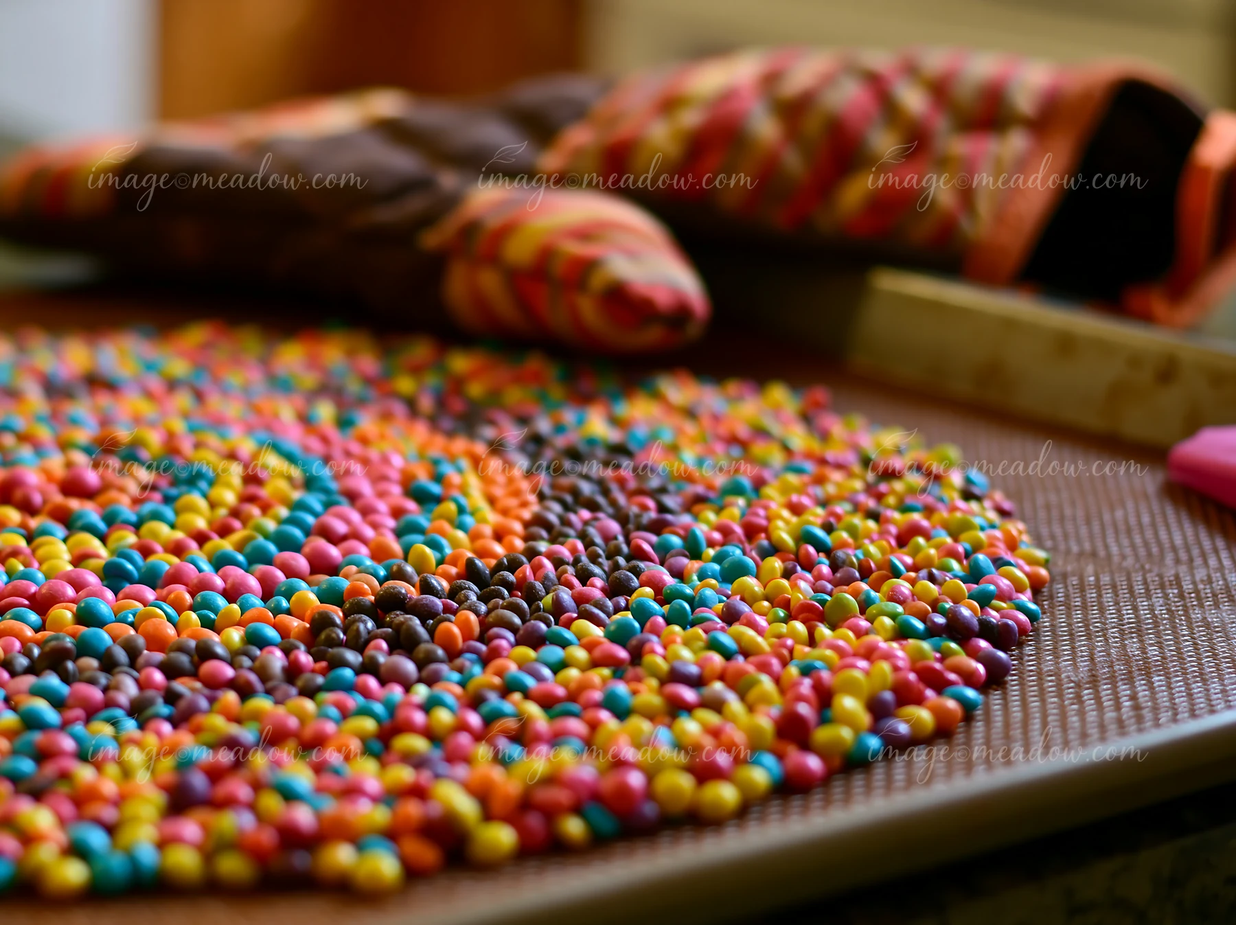 Colorful candy pieces forming spiral pattern on a woven mat next to a baking mitt.