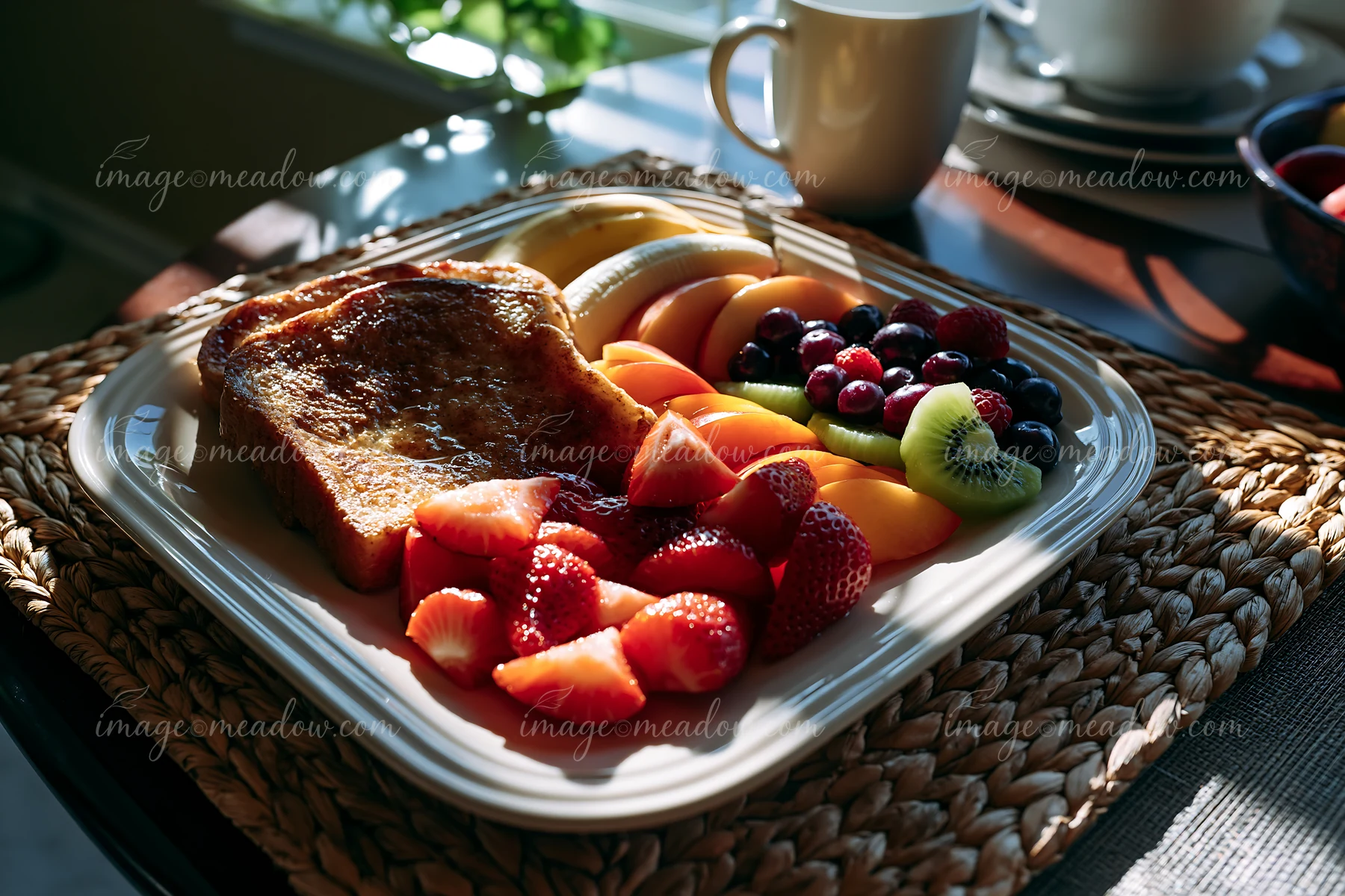 Colorful fruits are arranged on a plate beside a window with sunlight.