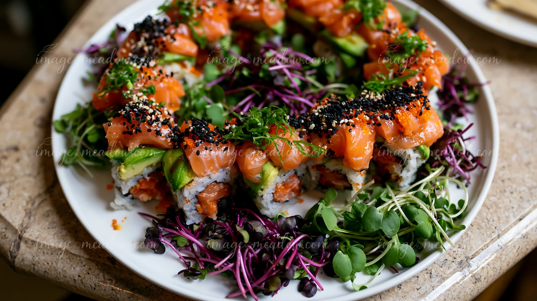 Colorful sushi rolls topped with salmon and avocado are served on a plate with fresh microgreens.