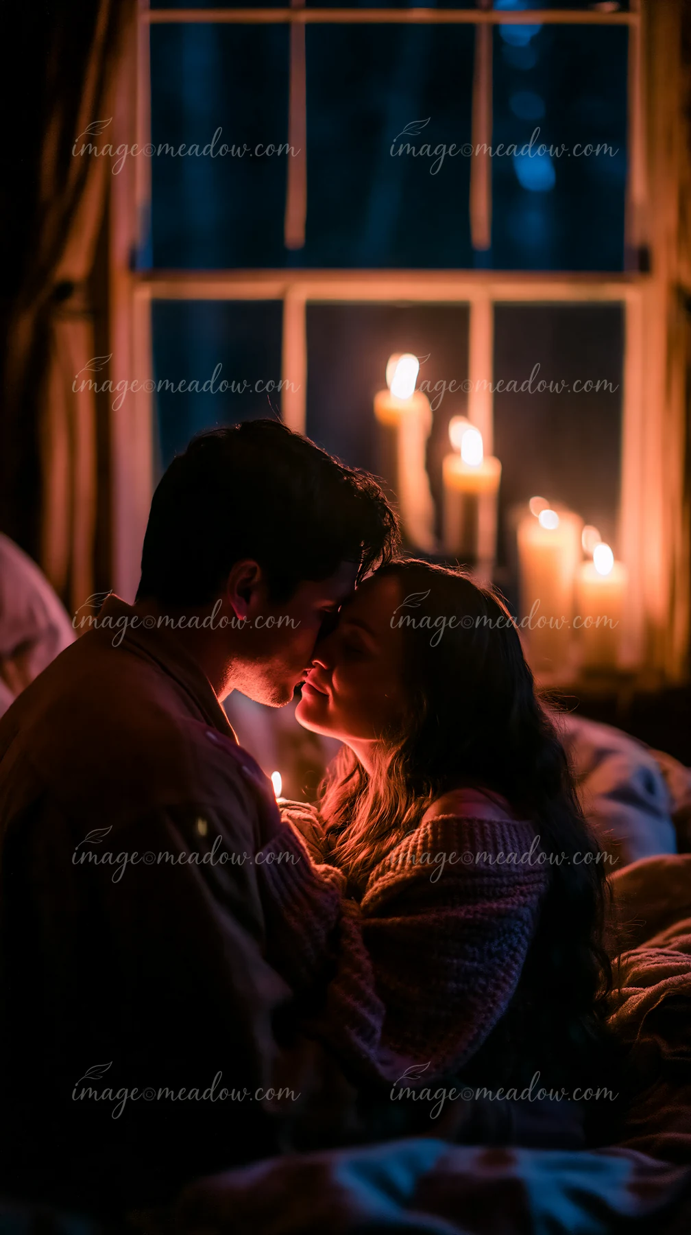 Couple embracing beside candlelight in a dim bedroom, sharing an intimate forehead kiss.