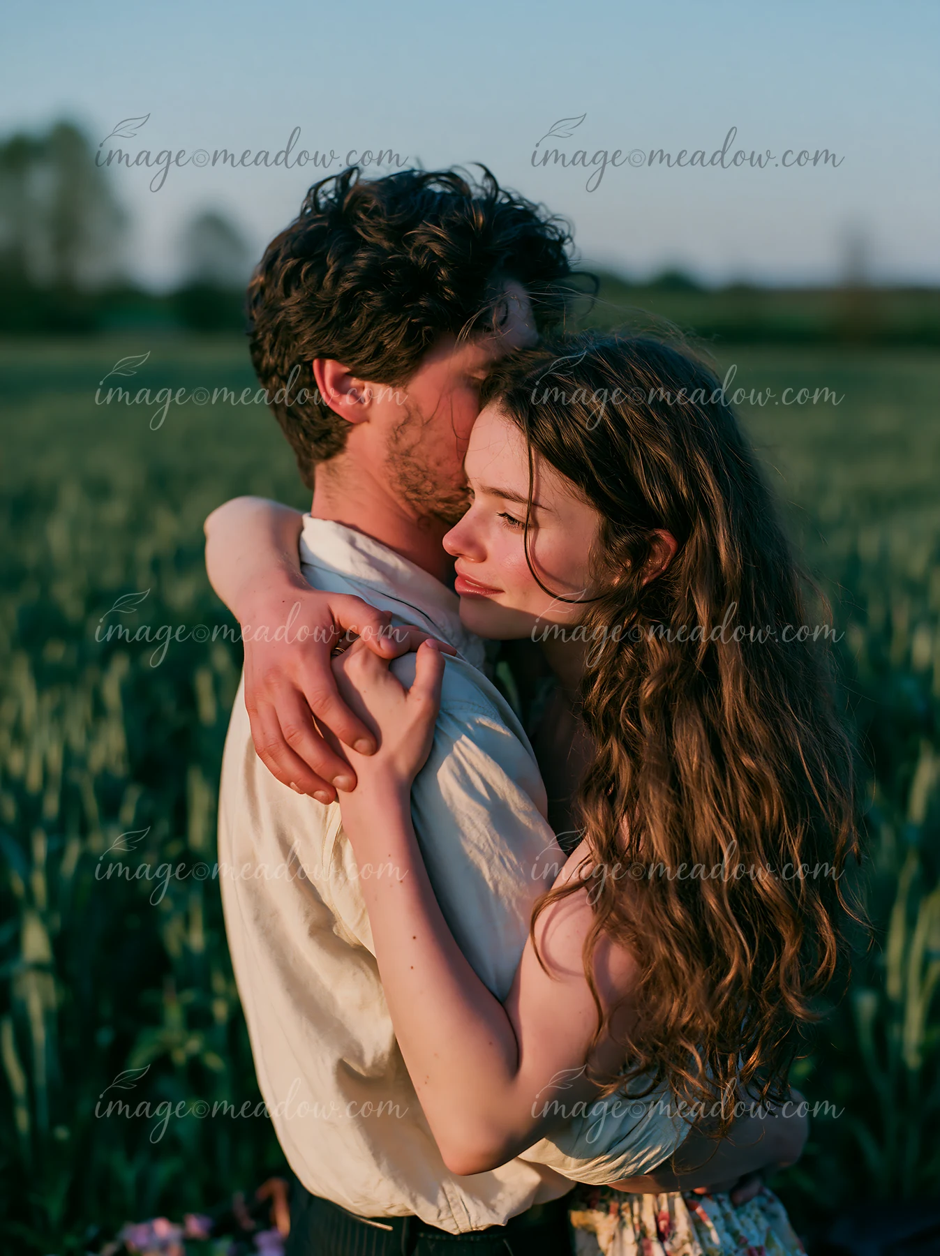 Couple embracing closely in a sunlit green field during spring.