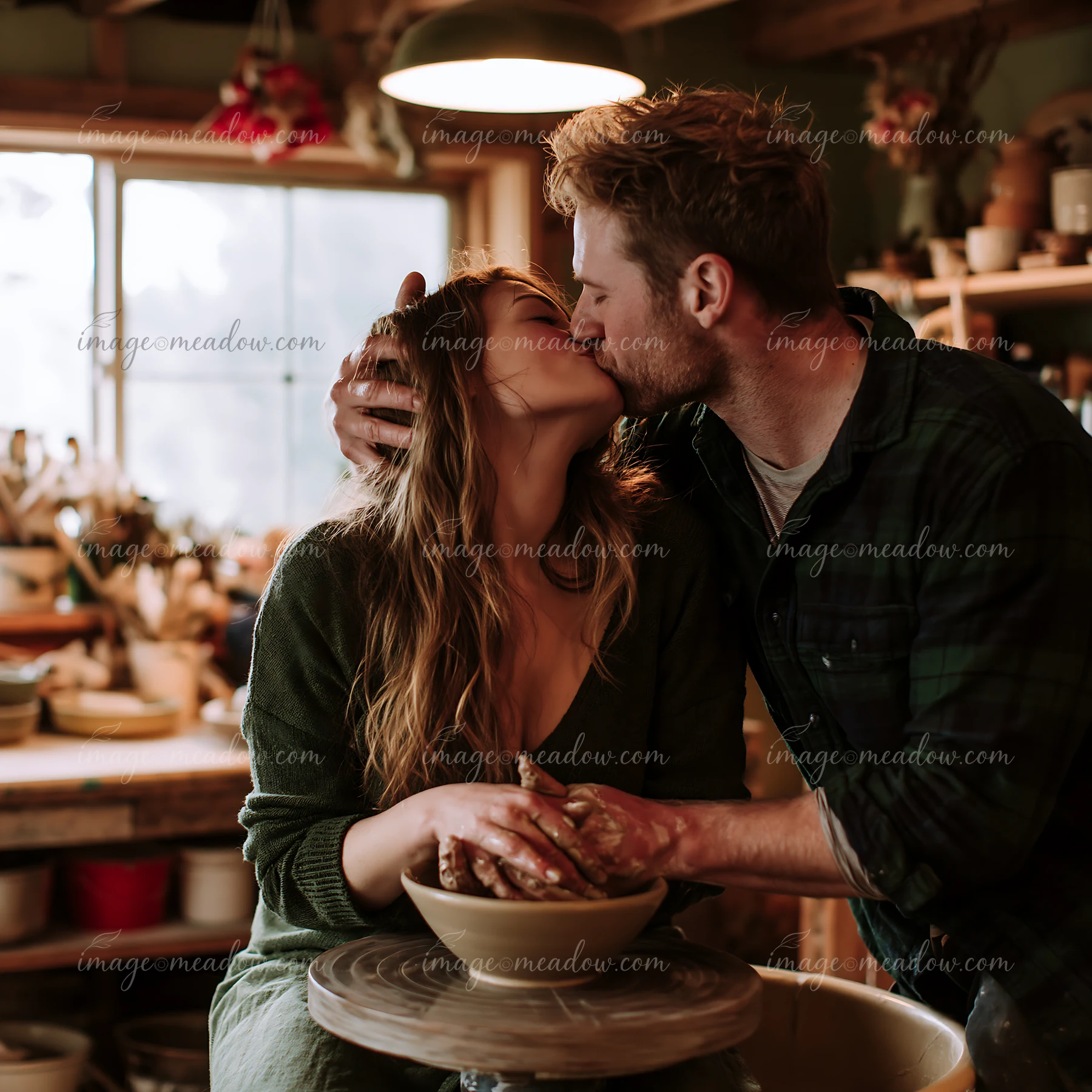 Couple kisses while making pottery together in a warmly lit ceramic studio.