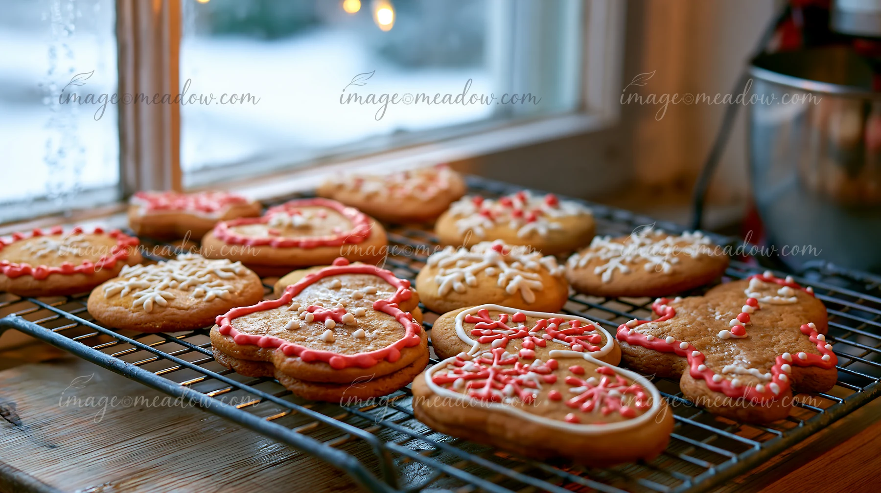 Decorated Christmas cookies cool on a wire kitchen rack beside a snowy window.