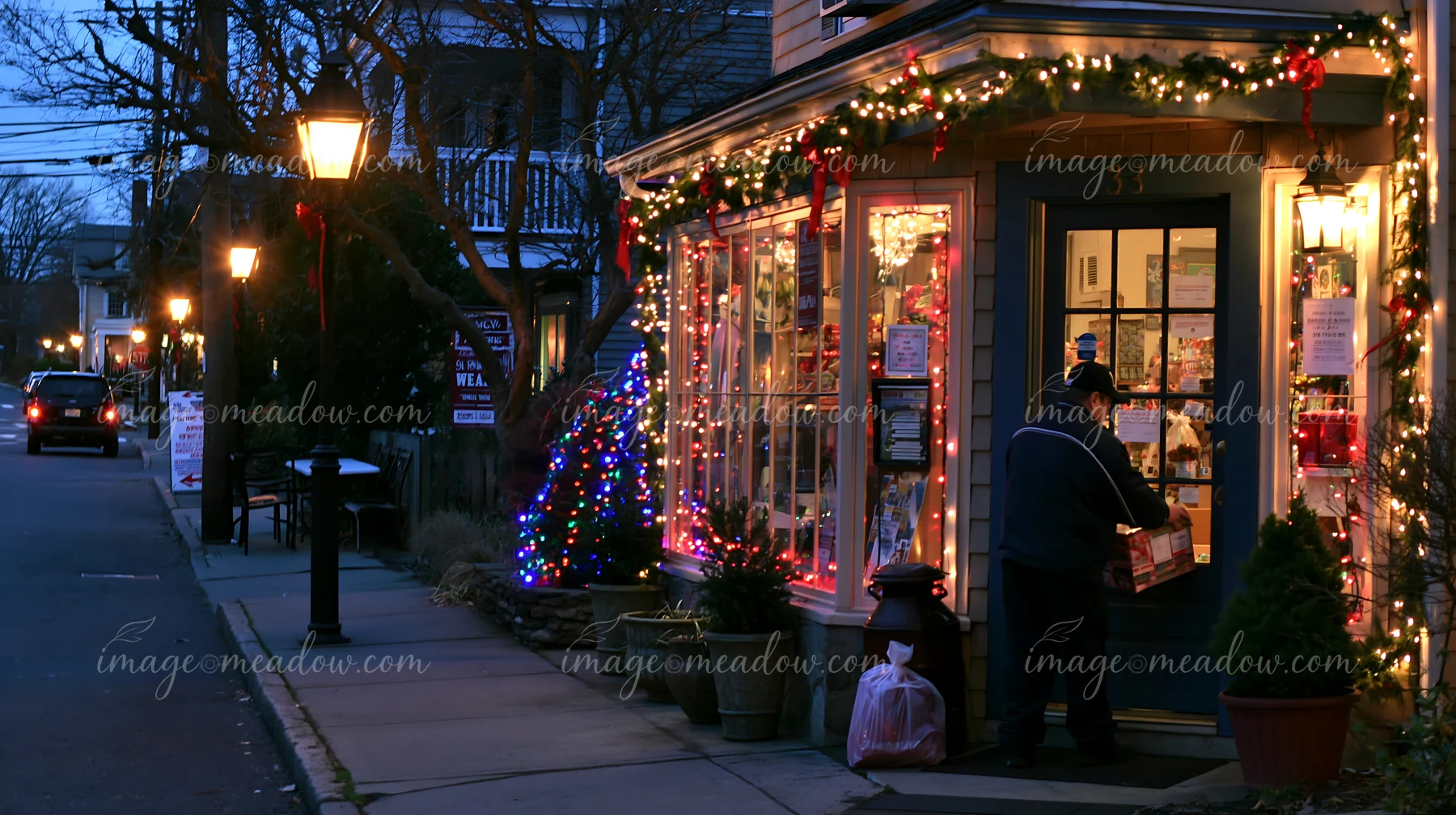 Delivery worker places a package at the doorstep of a Christmas-decorated storefront at dusk.