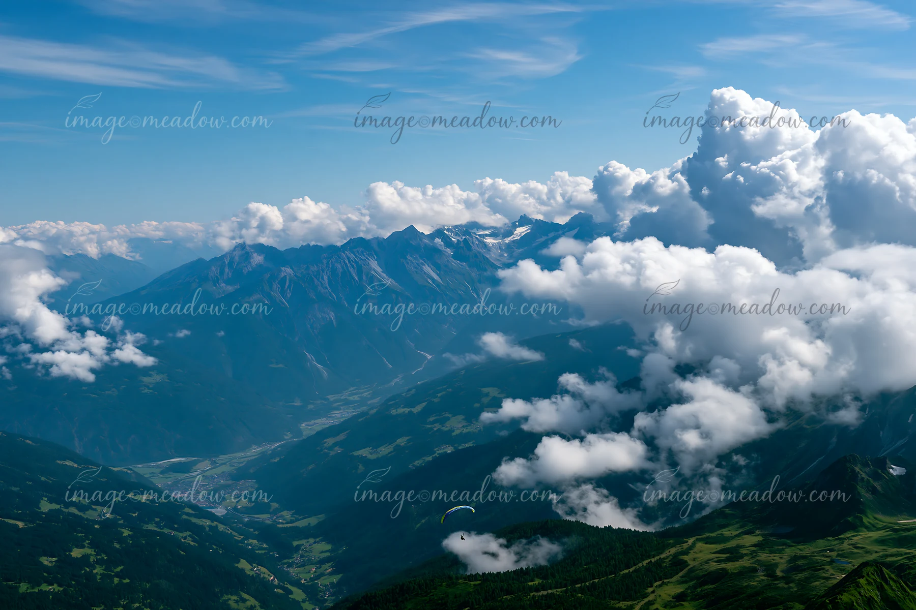 Dramatic clouds around alpine peaks fill the sky above green valleys.