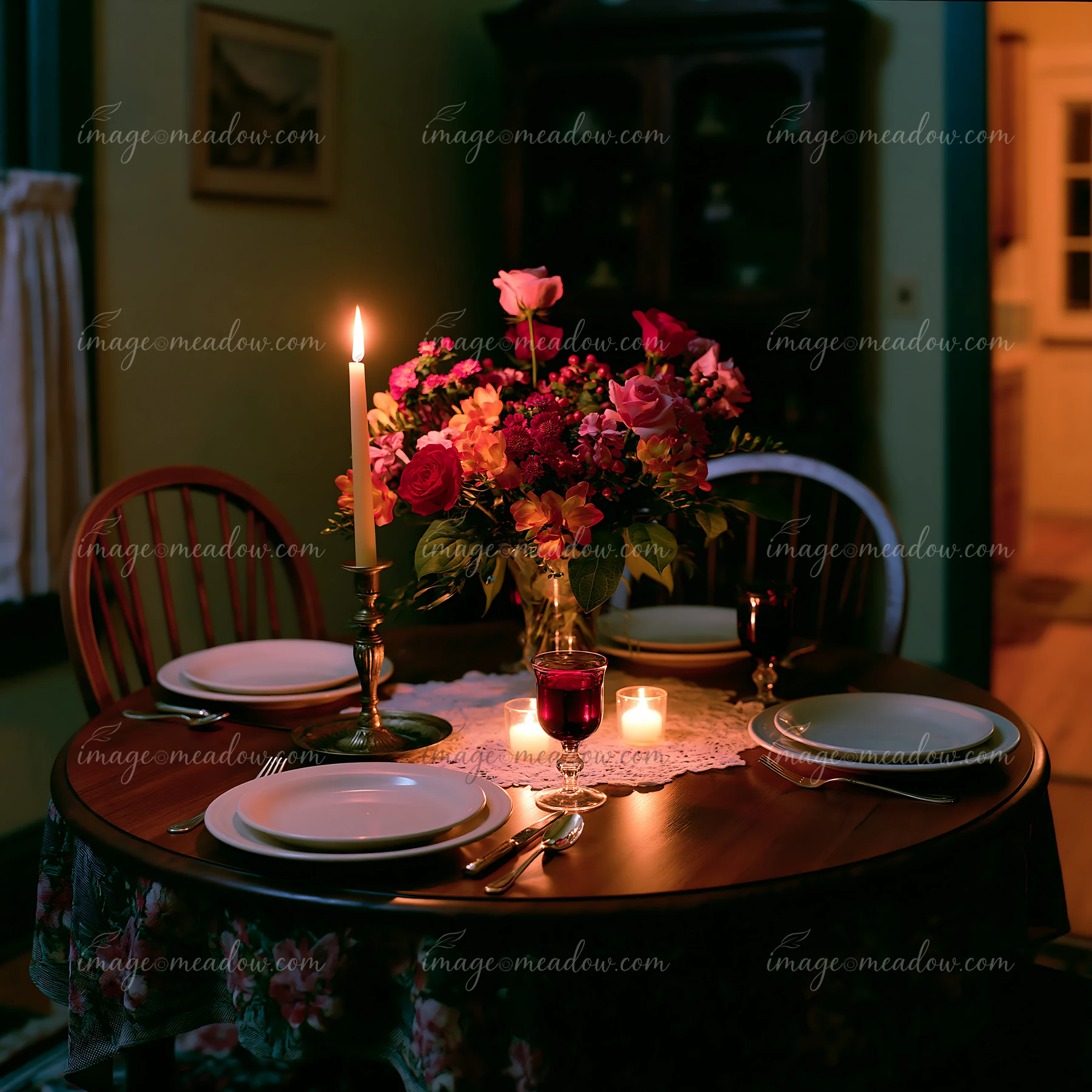 Empty dining chair beside sympathy flowers, candles, and a set dining table in a dimly lit room.