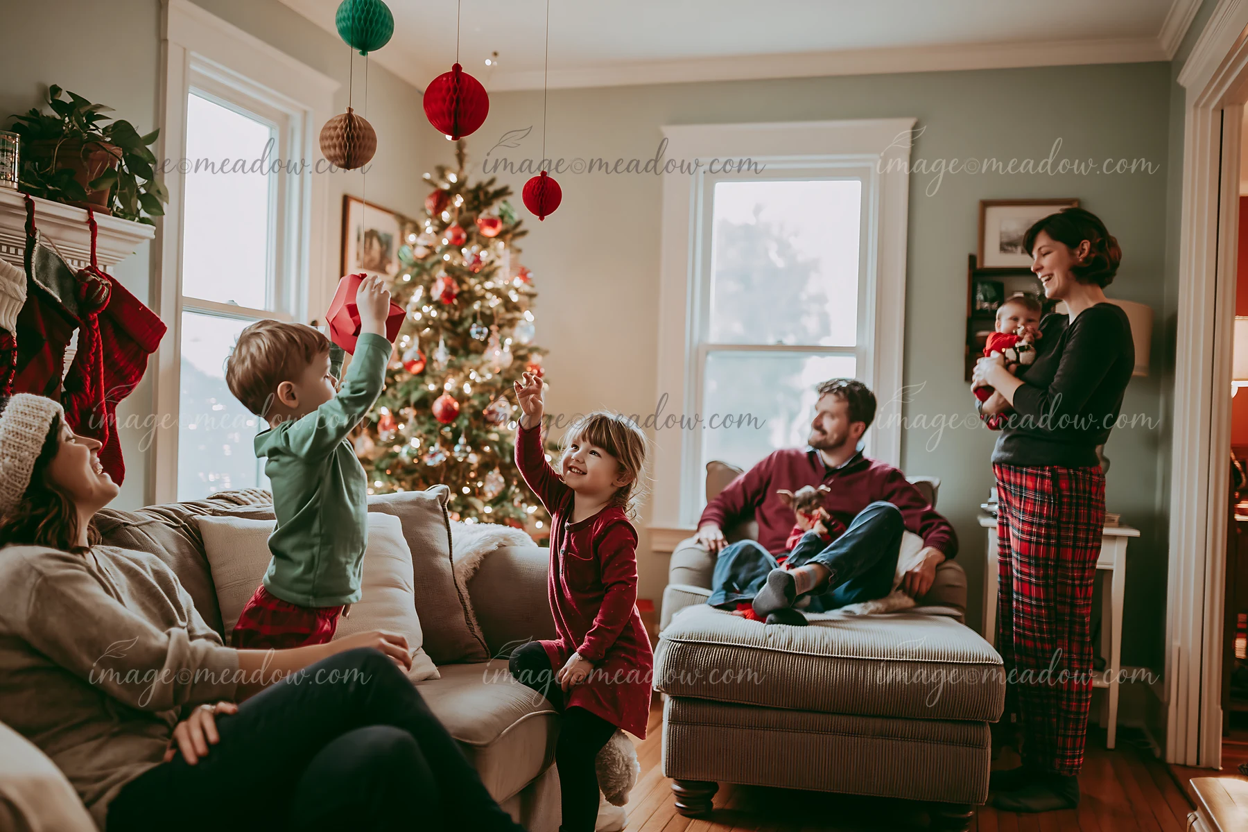 Family gathers around a decorated Christmas tree in a cozy living room during a festive holiday celebration.