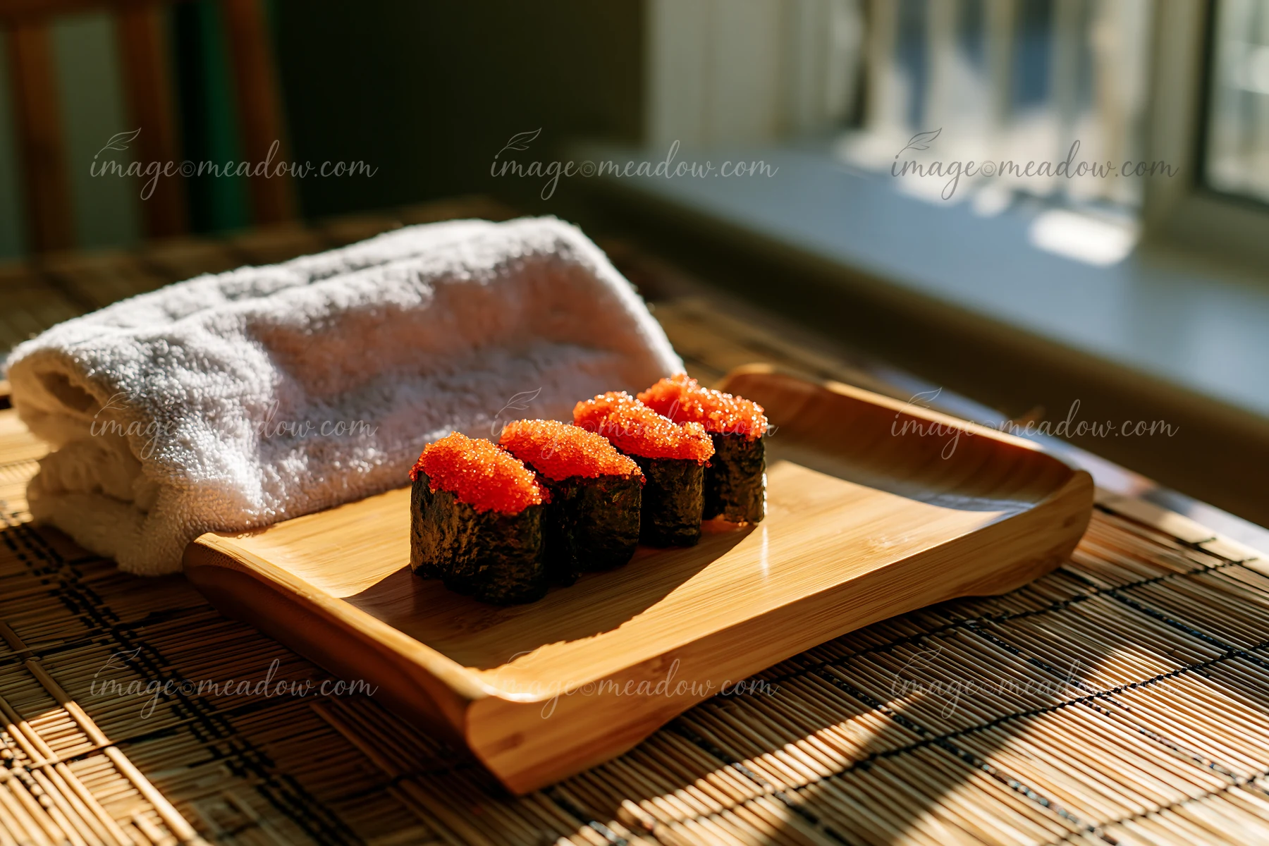 Four pieces of sushi with vibrant tobiko roe are neatly arranged on a wooden plate.