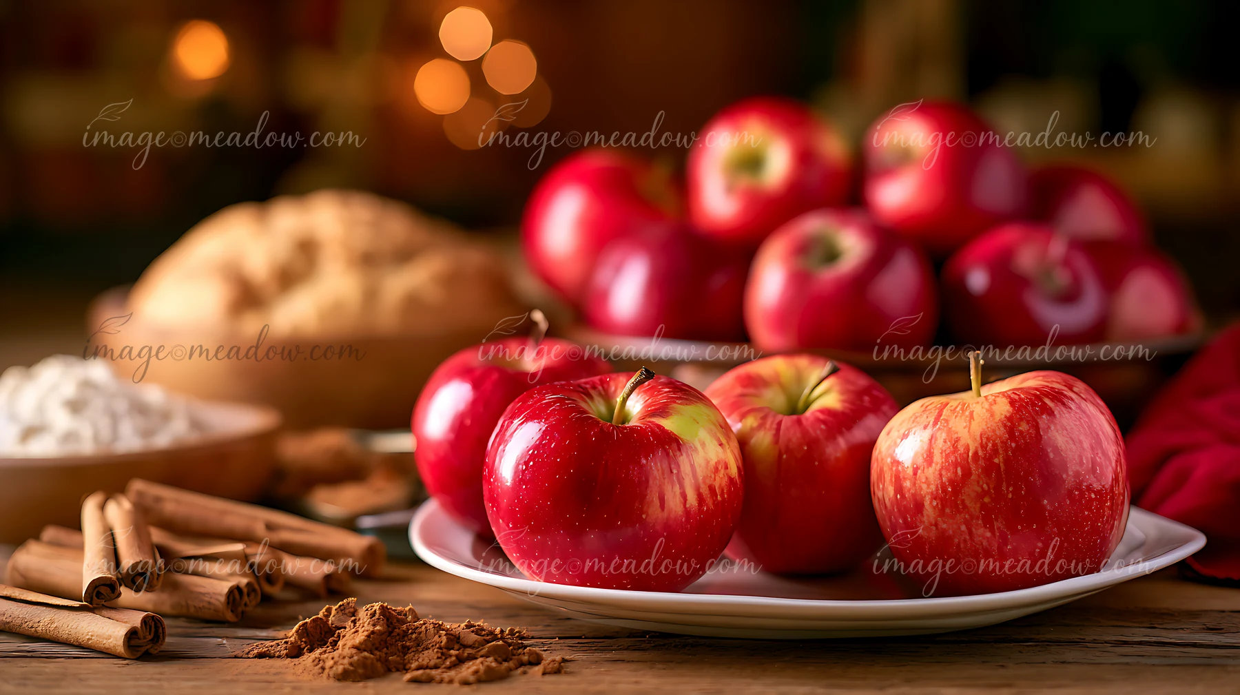 Fresh red apples sit on a plate next to a baked pie, a bowl of flour, and cinnamon sticks.