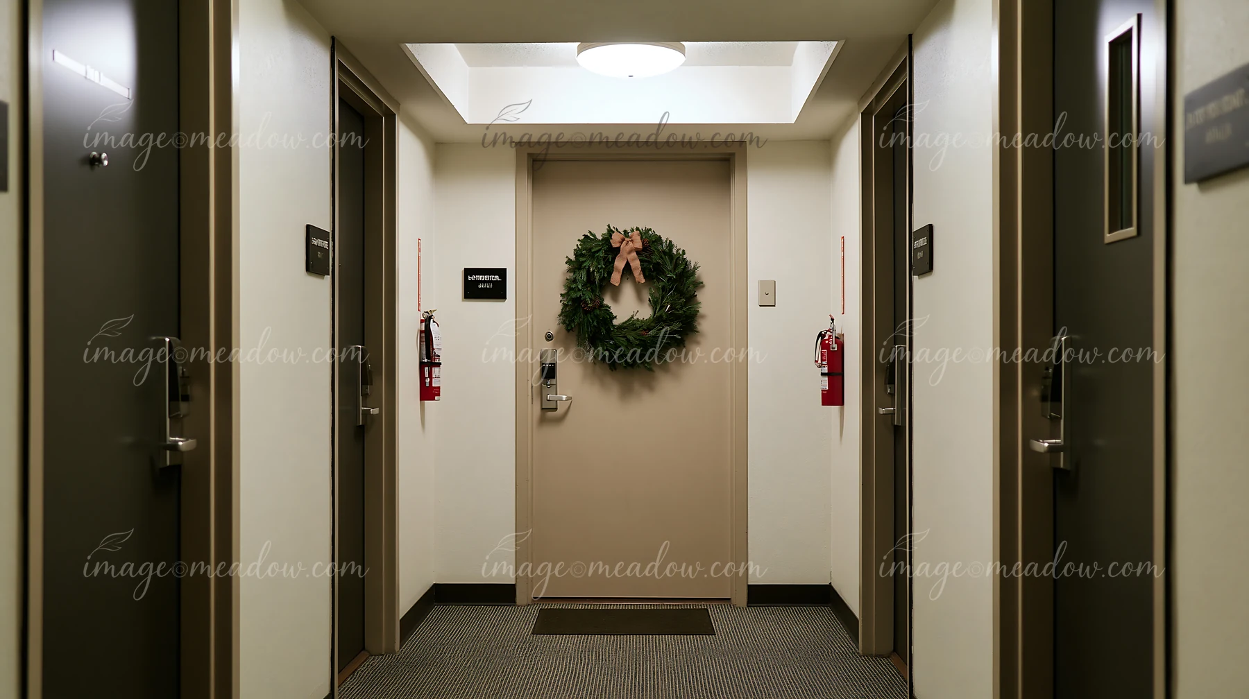 Green Christmas wreath with a bow hangs on an apartment door in a carpeted hallway.