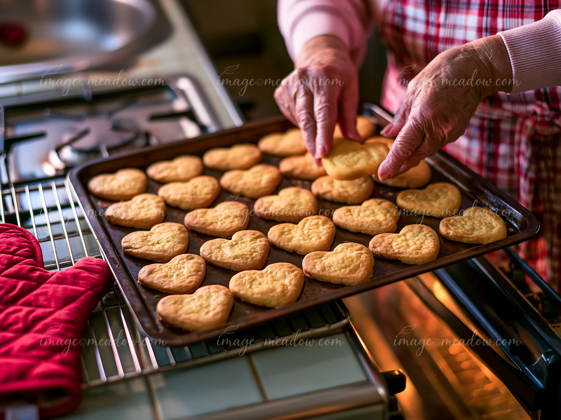 Hands are placing heart shaped cookies on a tray in a kitchen.