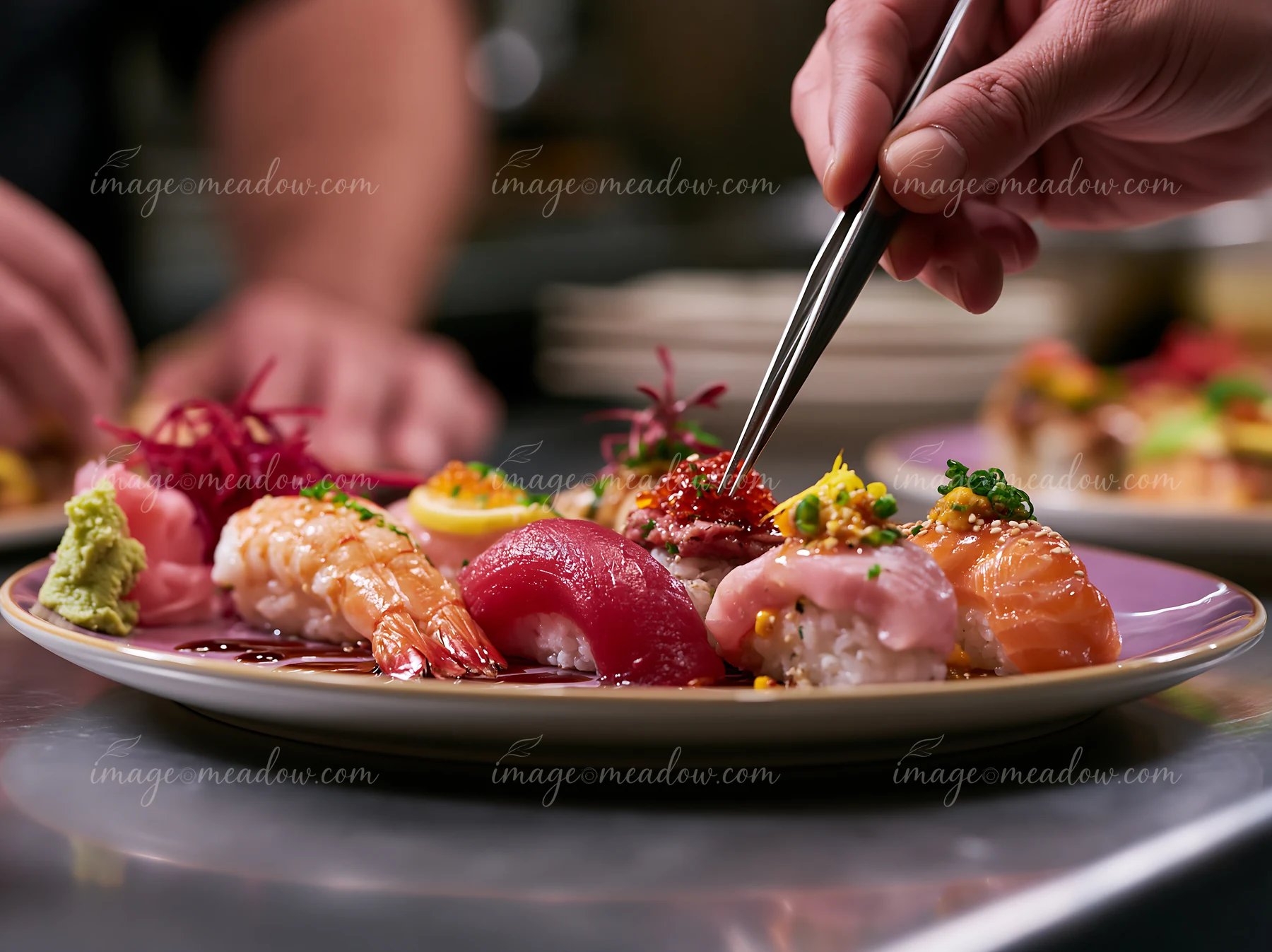 Hands are using chopsticks to select pieces from a colorful sushi platter.