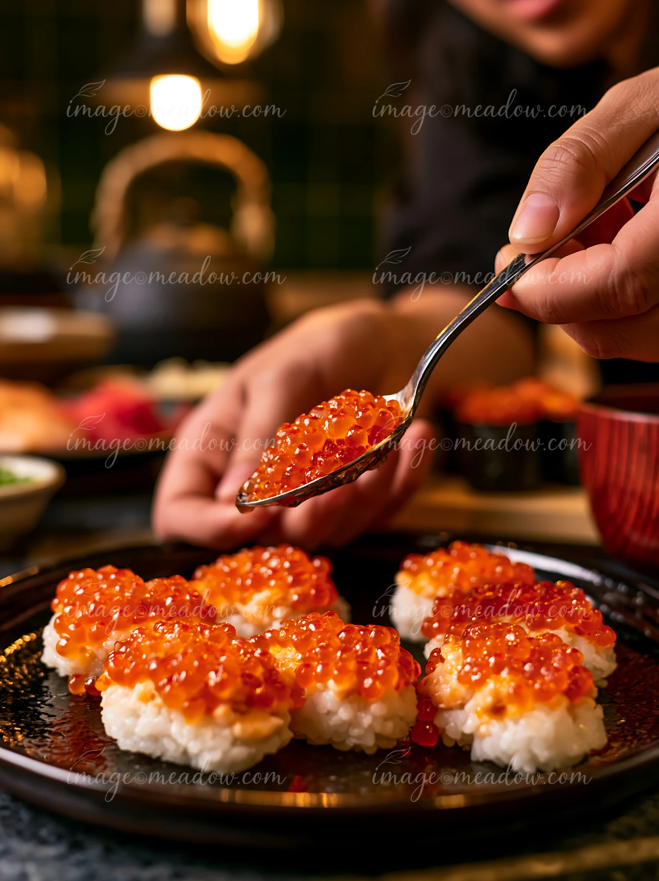 Hands placing roe on nigiri show detailed craftsmanship in a busy kitchen.