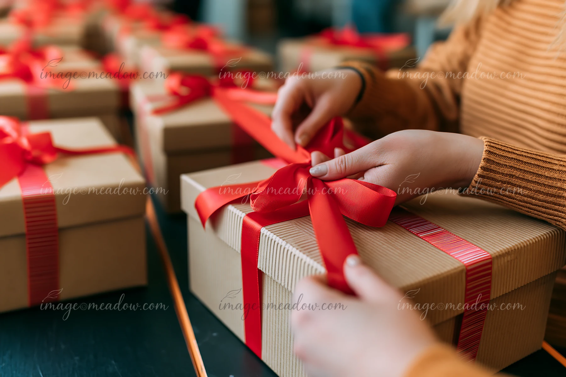 Hands tie a red ribbon around a gift box in a holiday setting filled with wrapped presents.