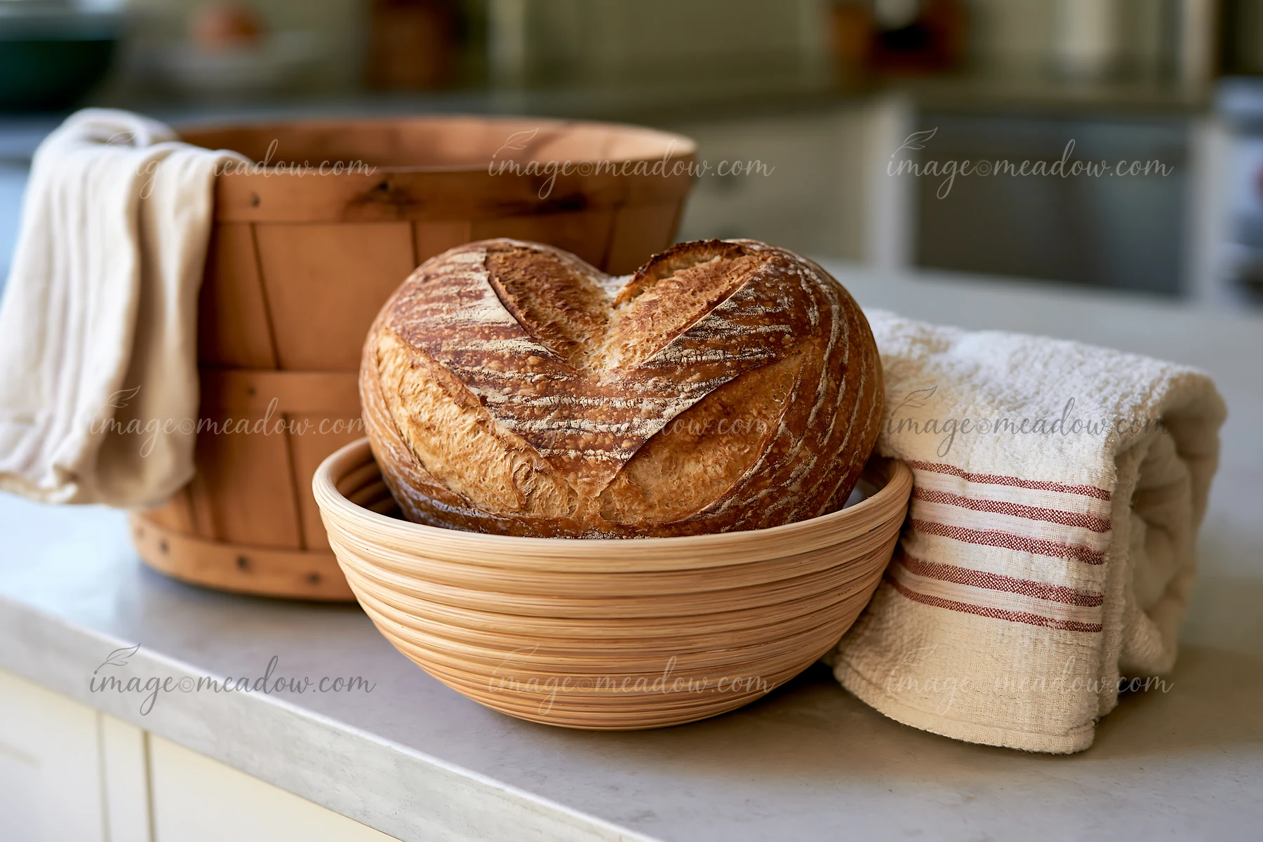 Heart-shaped artisan bread loaf rests in a woven basket on a kitchen counter beside a striped towel.