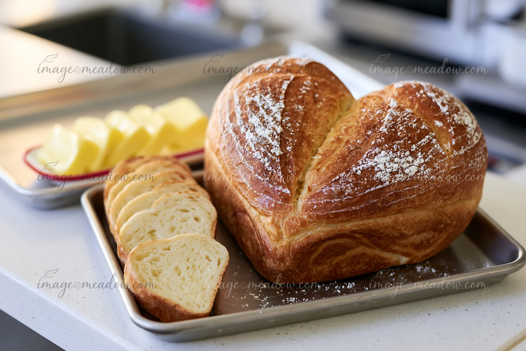 Heart-shaped bread loaf with sliced pieces on a metal tray beside butter on a kitchen counter.
