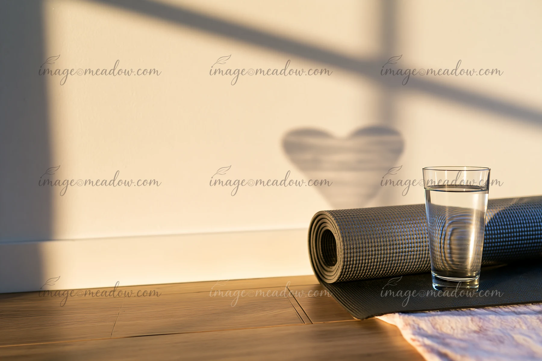 Heart-shaped shadow from window light falls on a wall beside a rolled yoga mat and glass of water.