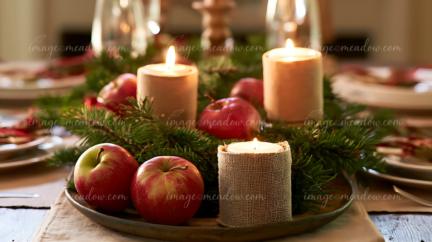 Lit candles, red apples, and evergreen branches form a Christmas centerpiece on a dining table.