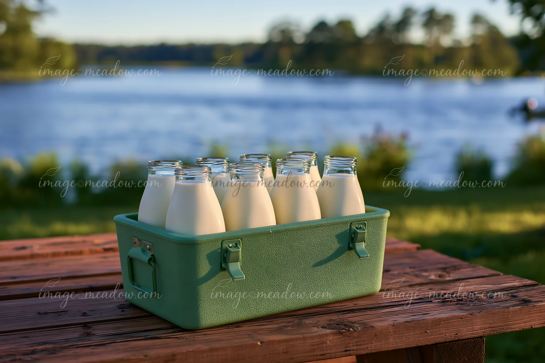 Milk bottles in an insulated delivery box sit on a wooden table by a lake.