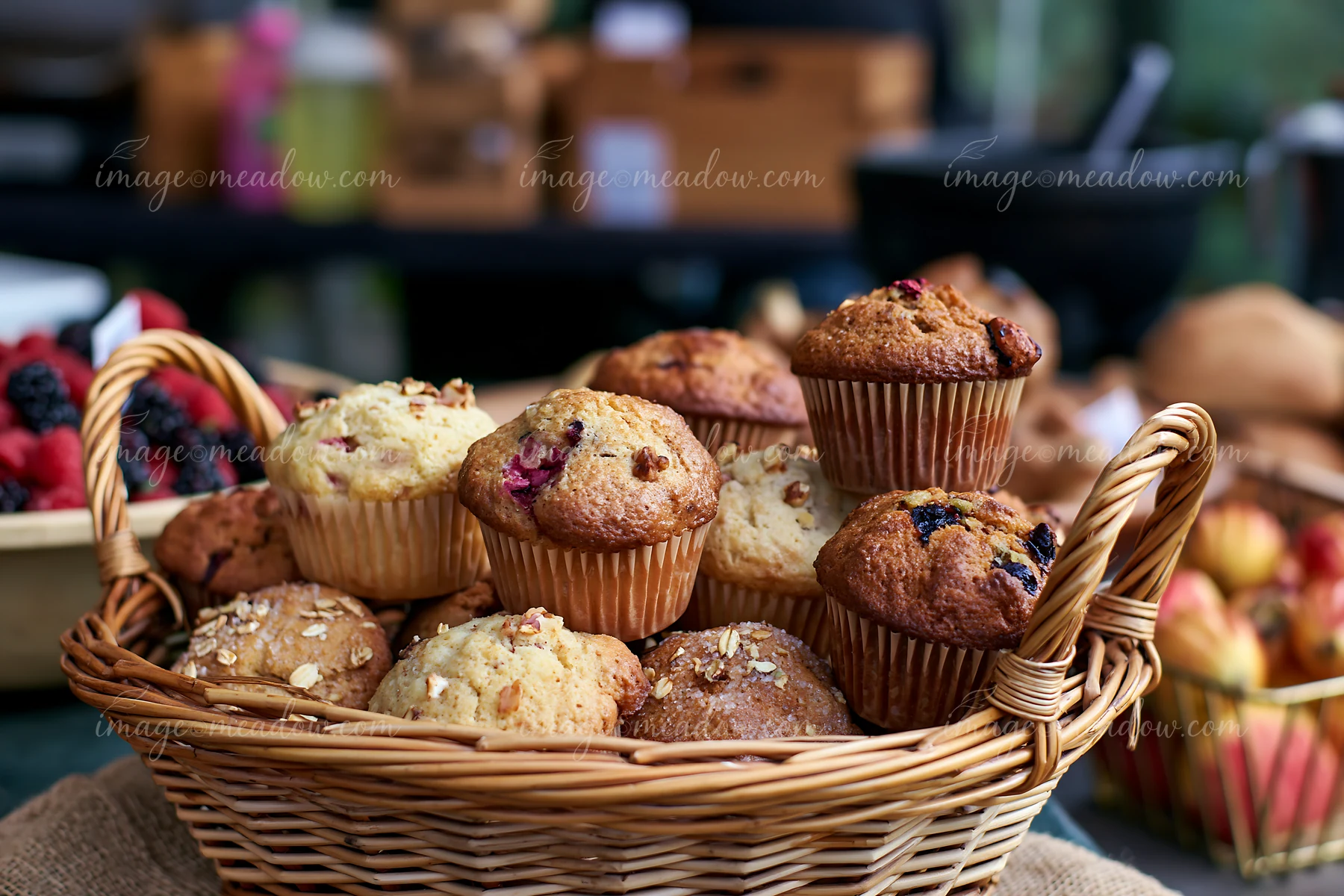 Muffins are arranged in a basket at a bakery with other baked goods seen in the background.