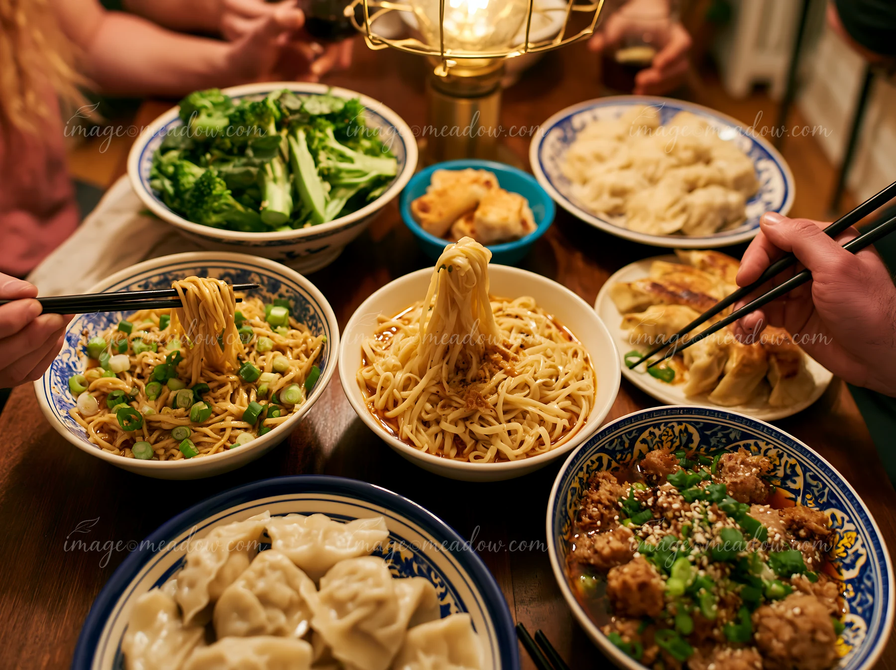 Noodles, dumplings, and vegetables are shared around a table at a gathering.