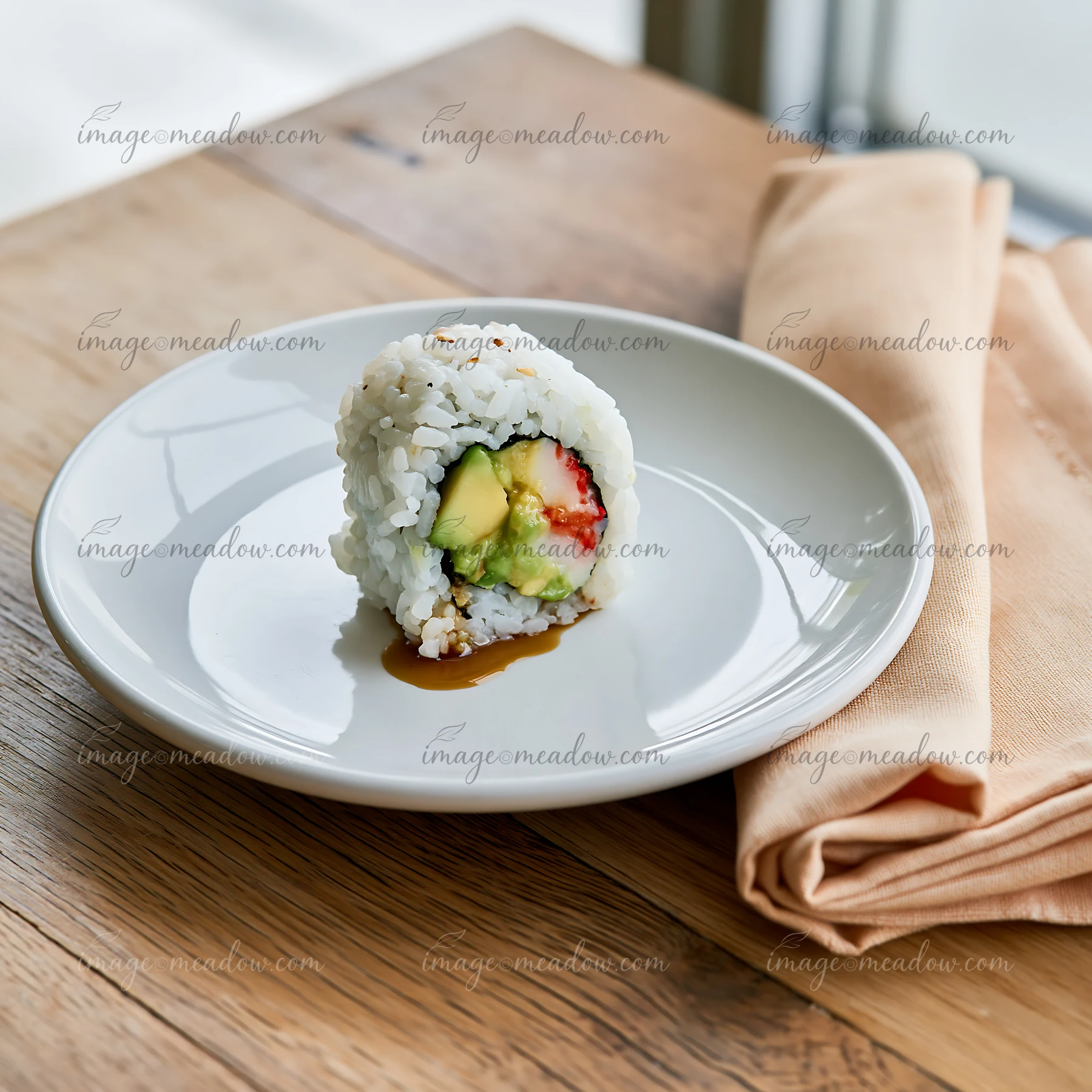 One California roll piece on plate sits on a wooden table near a folded napkin.