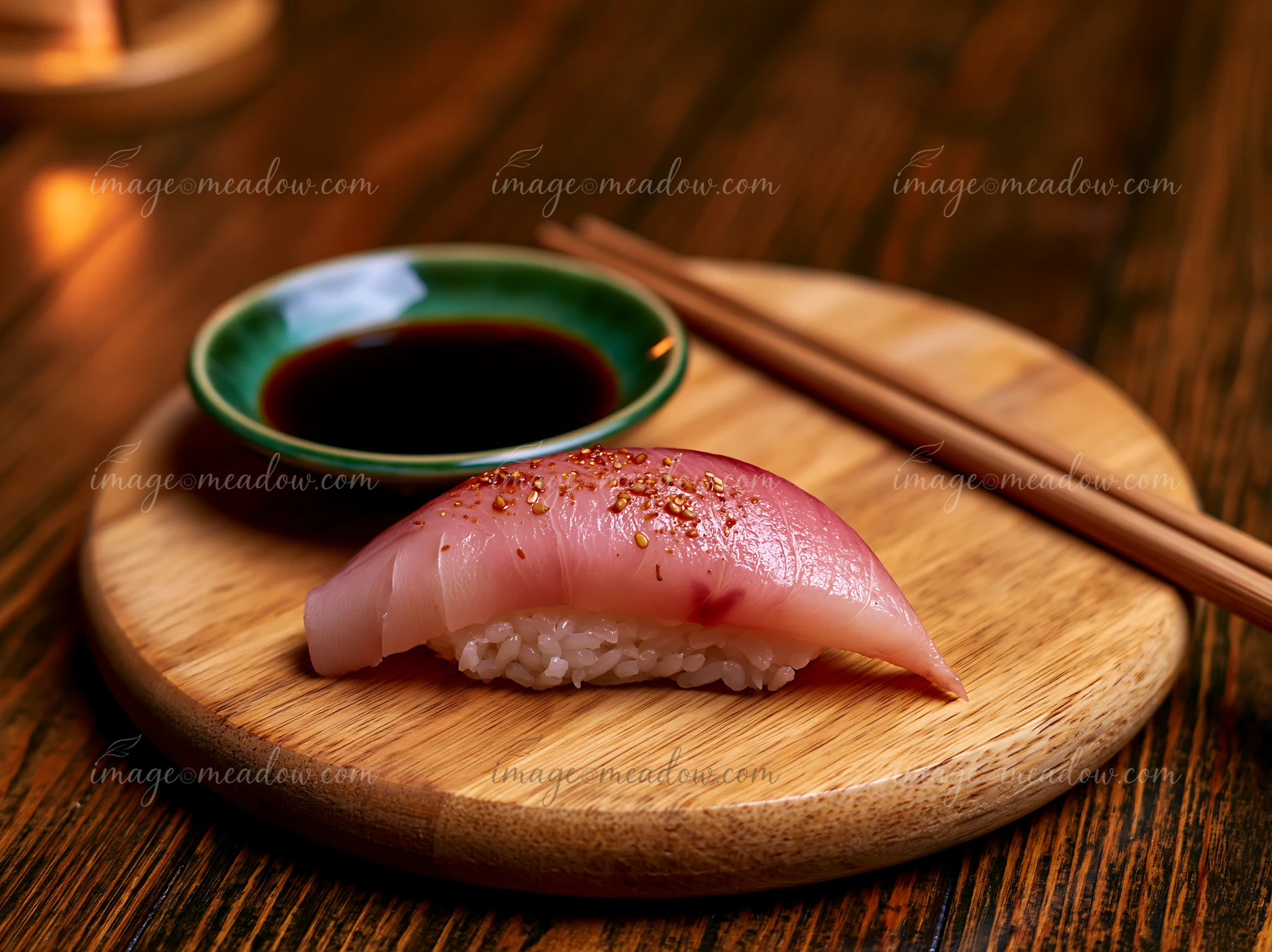 One nigiri beside soy sauce dish is placed on a wooden platter with chopsticks resting beside it.