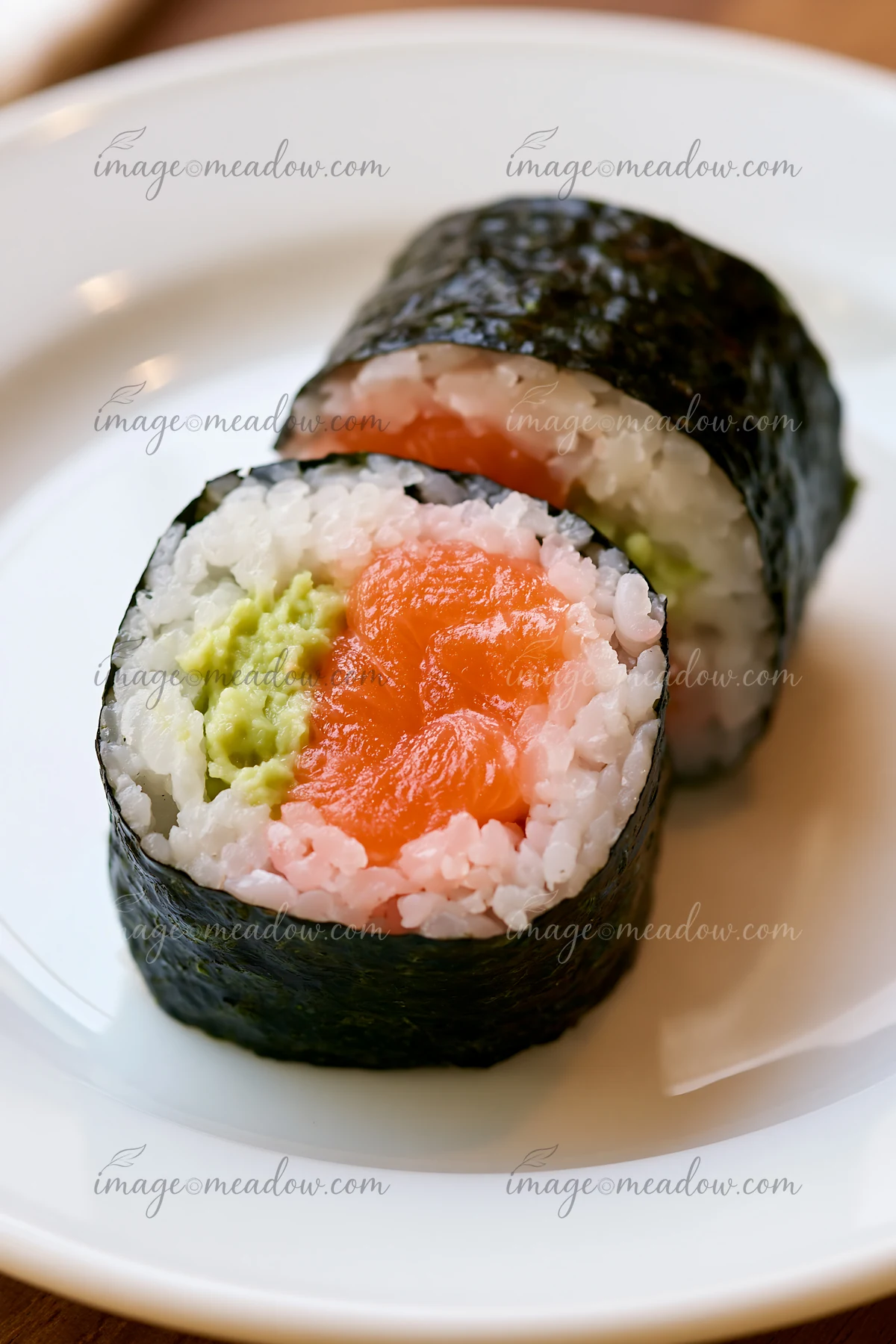 One salmon maki piece with wasabi is displayed on a white plate.