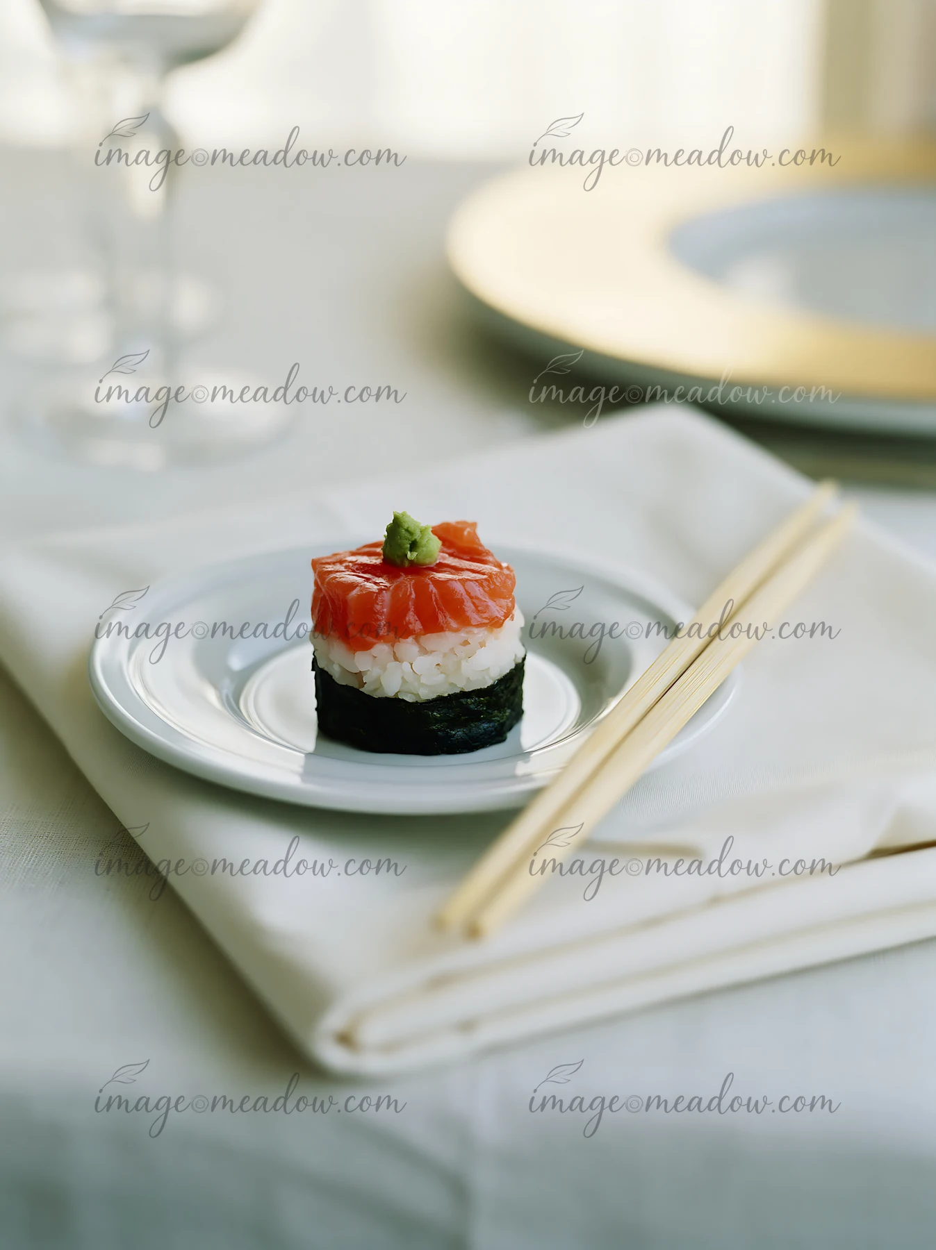 One salmon maki piece with wasabi is placed on a small white plate.