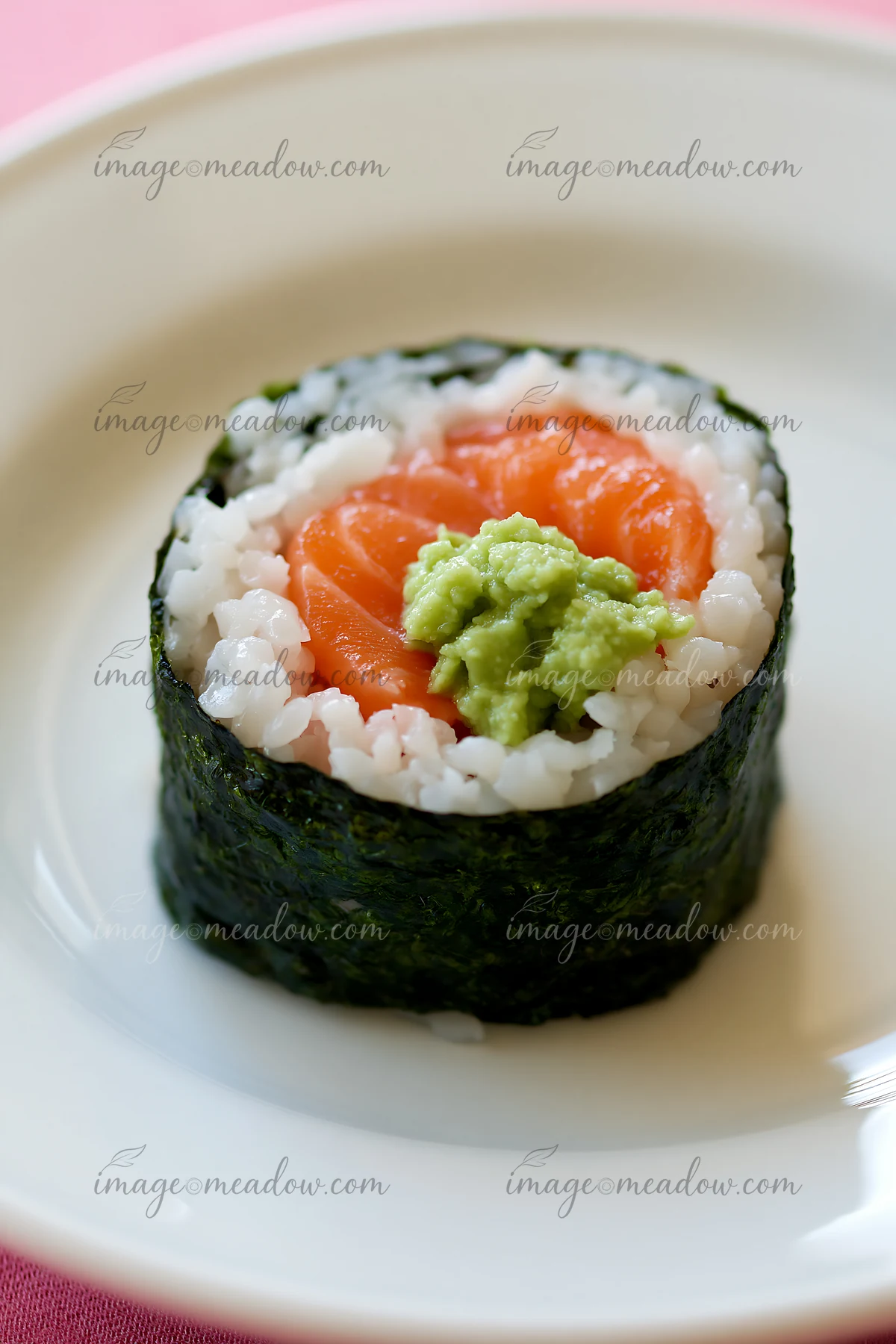 One salmon maki piece with wasabi sits on a white plate.