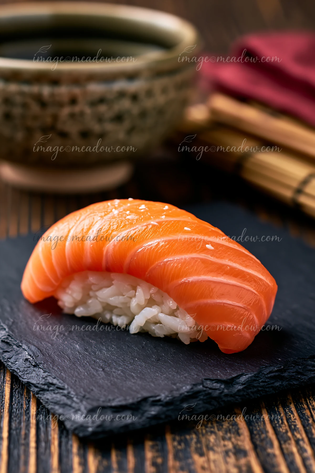 One salmon nigiri on slate plate sits on a wooden table.