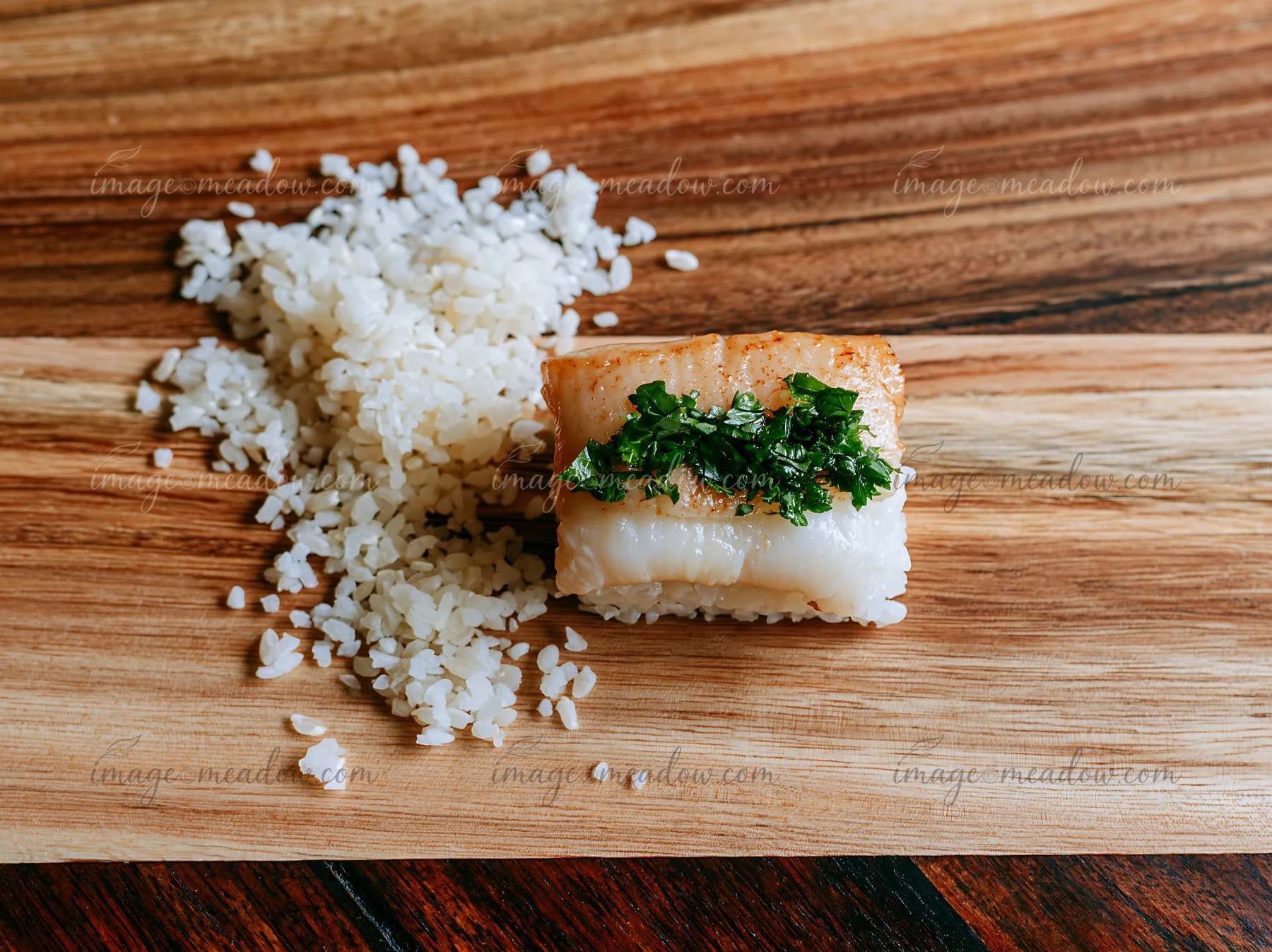 One sushi piece with fresh herb garnish sits next to a small mound of rice on a wooden board.