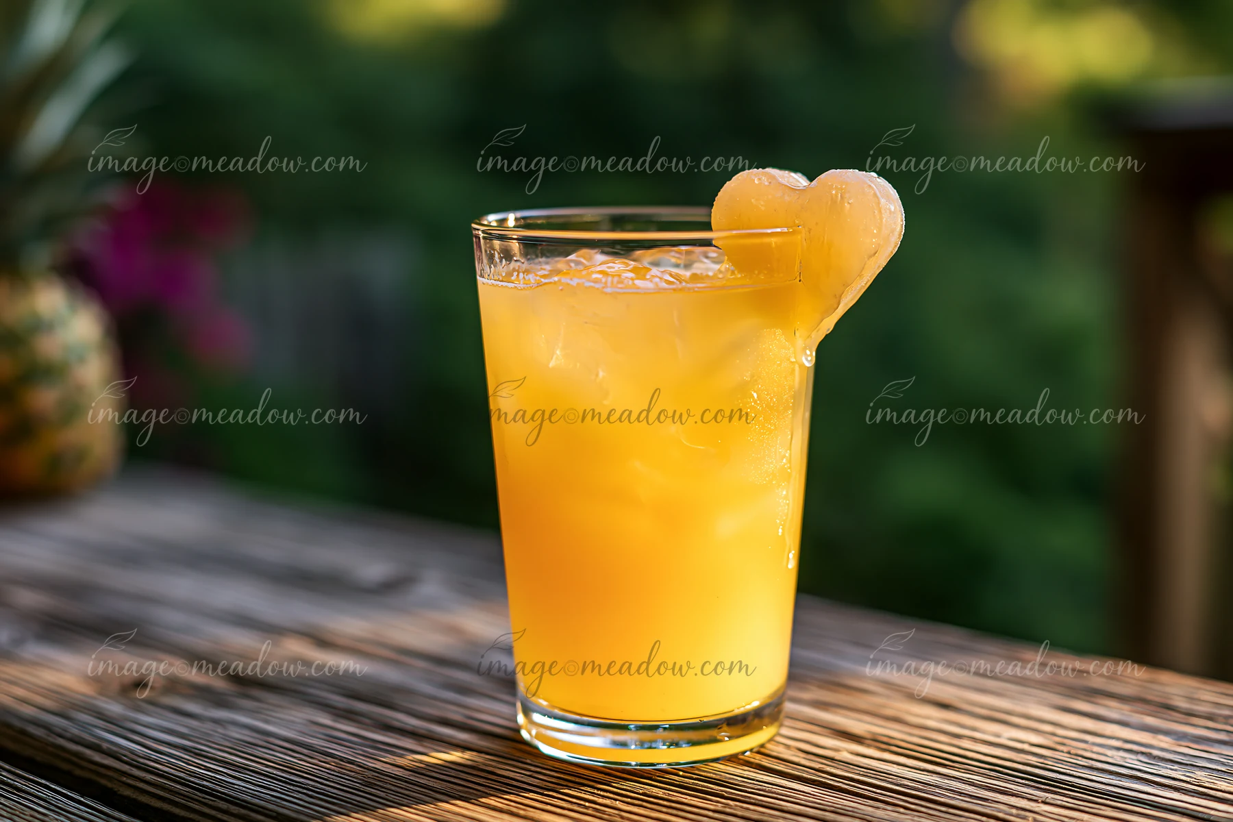 Orange drink in a clear glass with a melting heart-shaped ice cube on a wooden outdoor table.