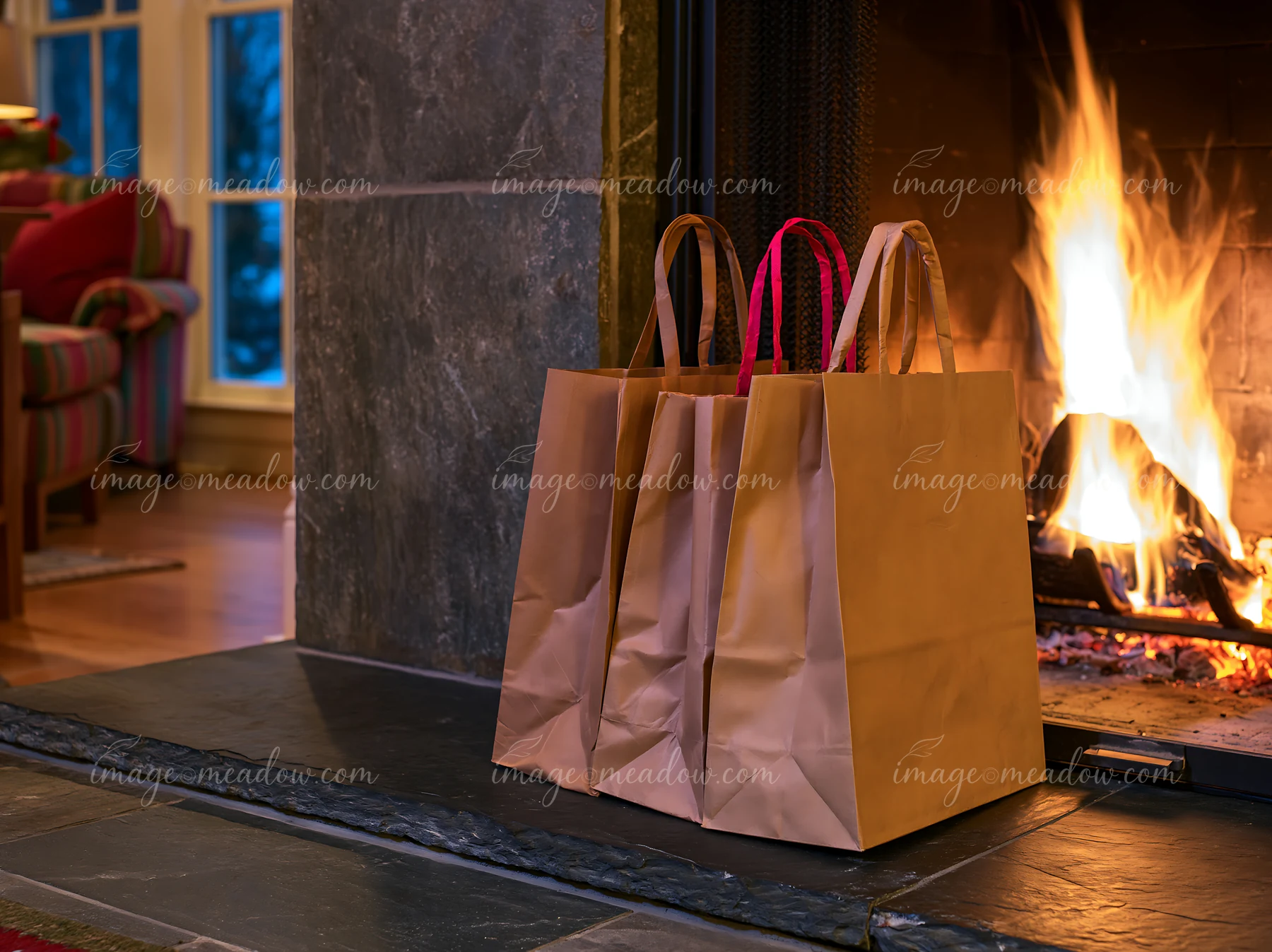 Paper shopping bags sit beside a glowing fireplace, with wrapped gifts and a window in the background.