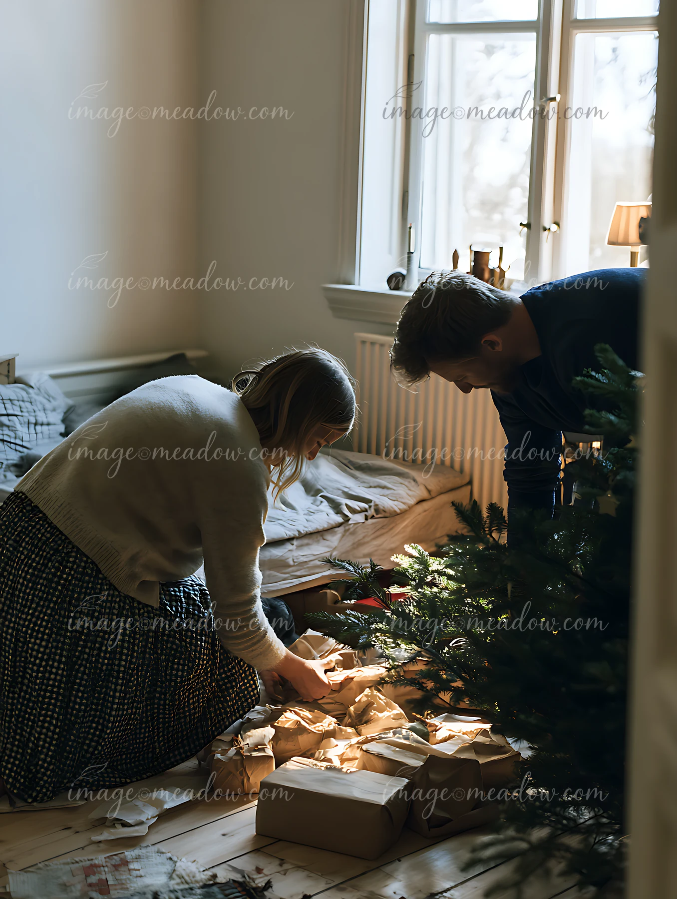 Parents are arranging gifts under a Christmas tree in a cozy living room.