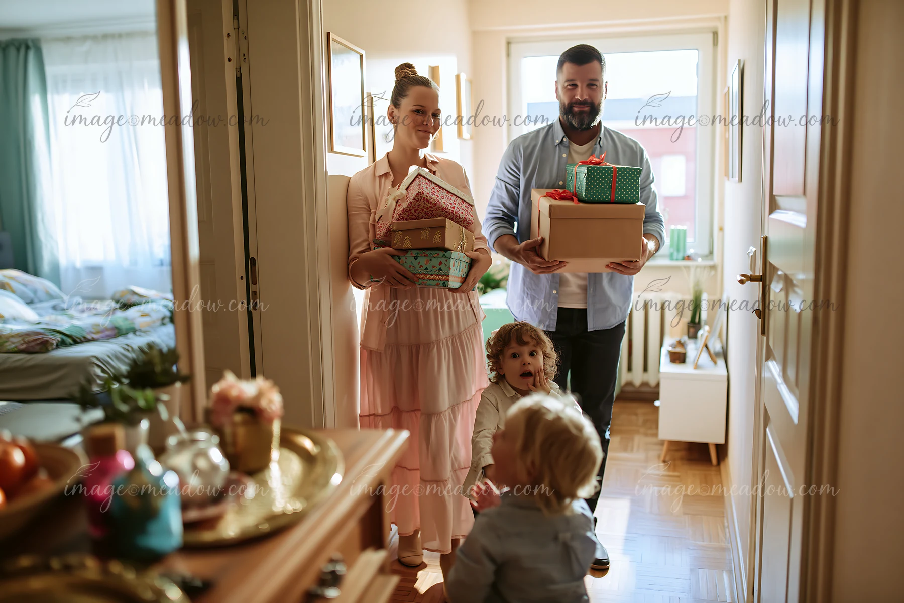 Parents carry decorated gift boxes into a bright home while three children greet them.