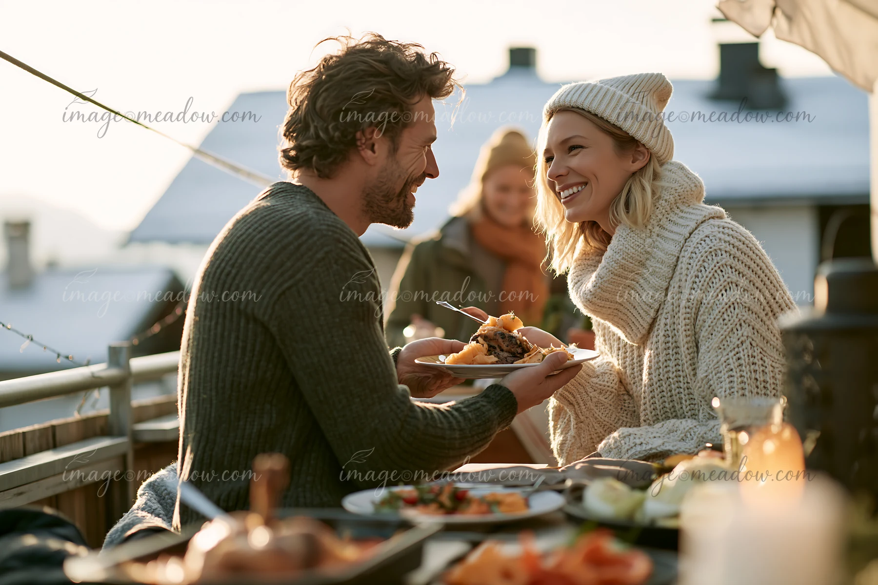 Parents serve a festive meal to each other at an outdoor table in winter clothing.