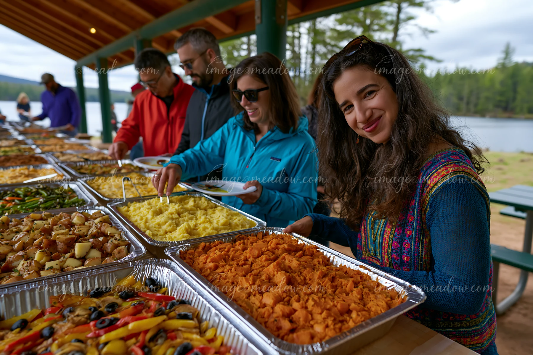 People enjoy a variety of dishes at a buffet table near a lake.