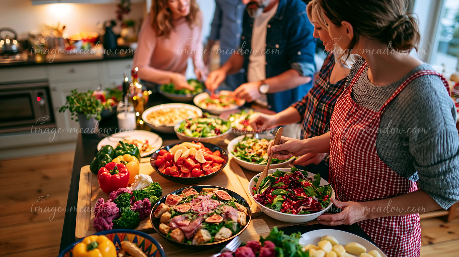 People prepare a Christmas dinner in a kitchen with various salads and vegetables on the table.