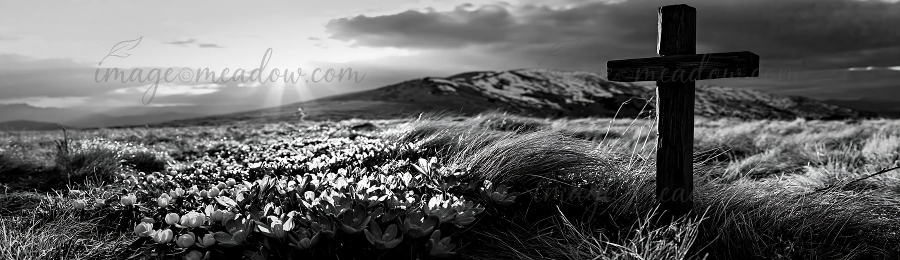 A rustic Christian cross stands in a winter meadow with snow-covered hills in the background. The sun sets behind the mountains, creating a dramatic sky filled