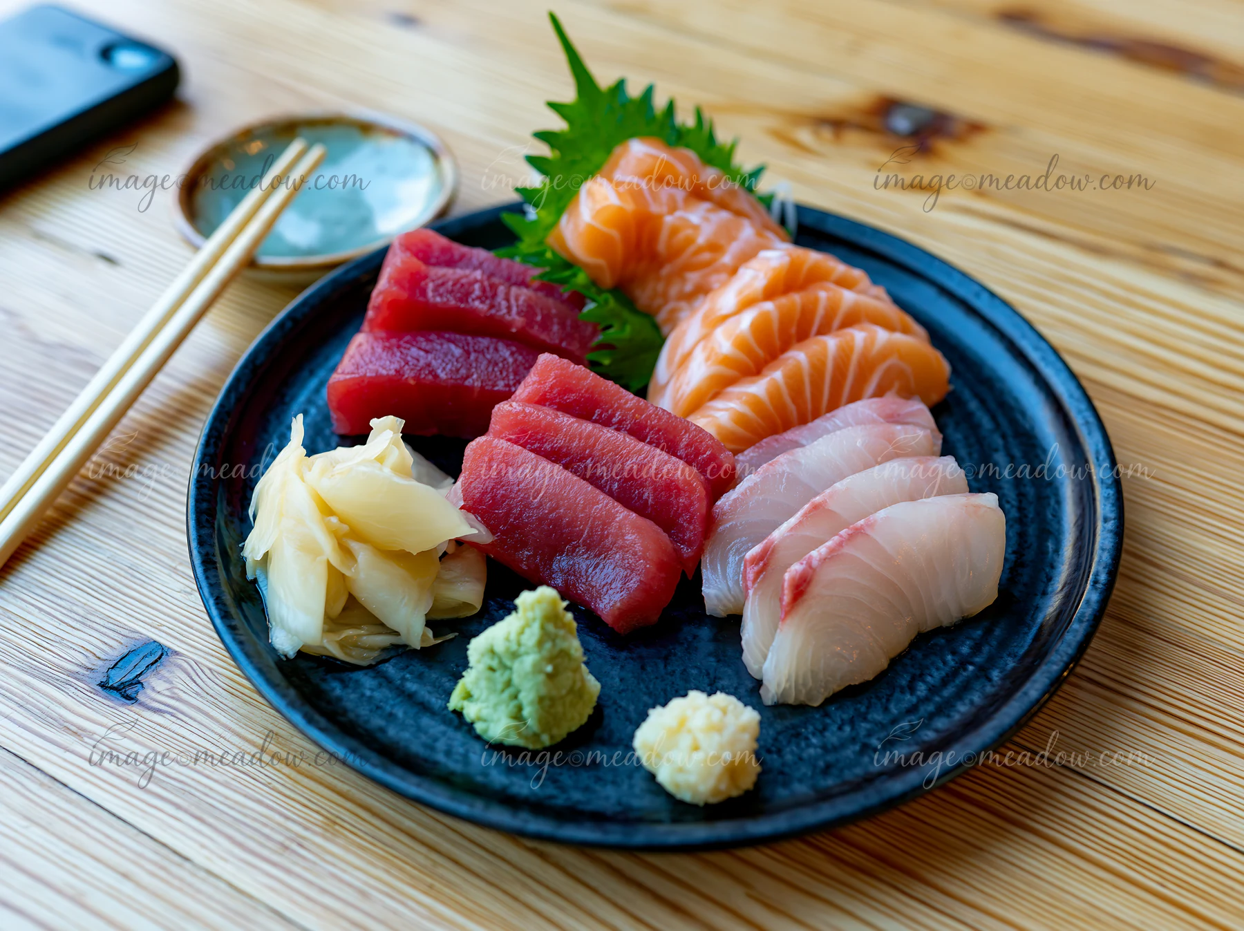 Sashimi platter with pickled ginger features slices of tuna, salmon, and white fish, arranged on a black dish.