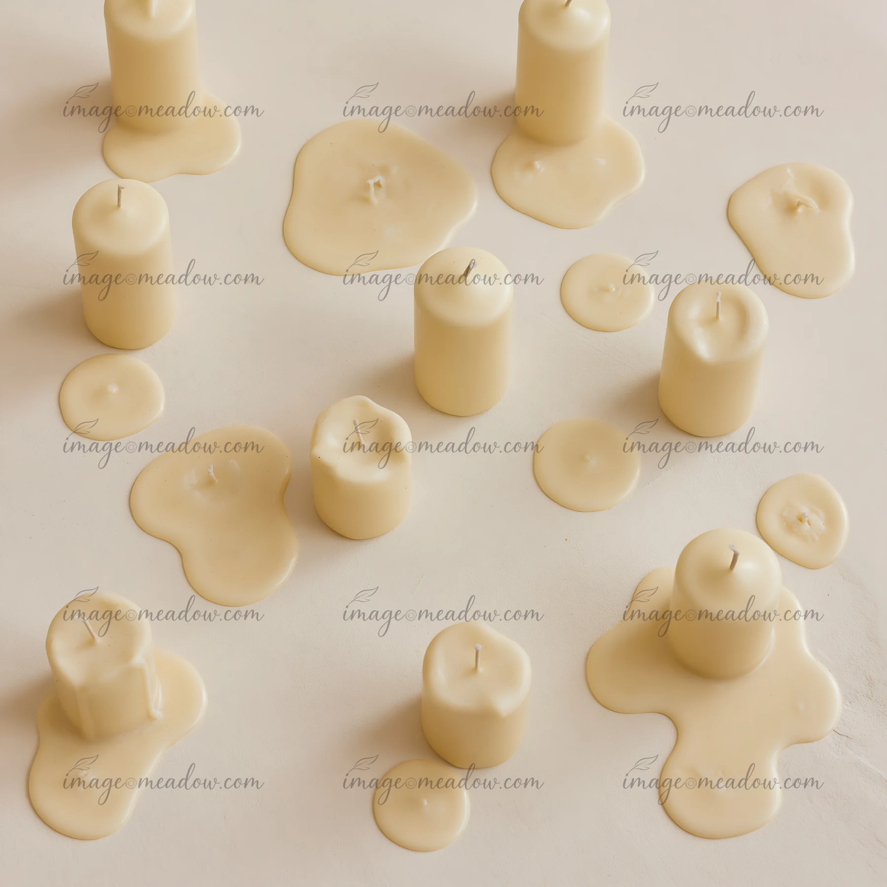 Several vanilla candles sit on a neutral surface, some lit and others with melted wax pooling around them.