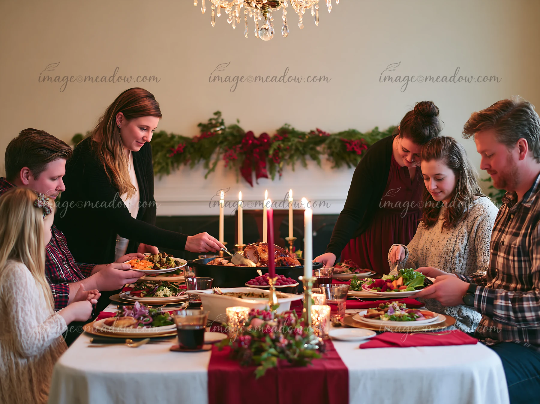 Six people share a festive holiday meal around a candlelit dining table with roasted food and vegetables.