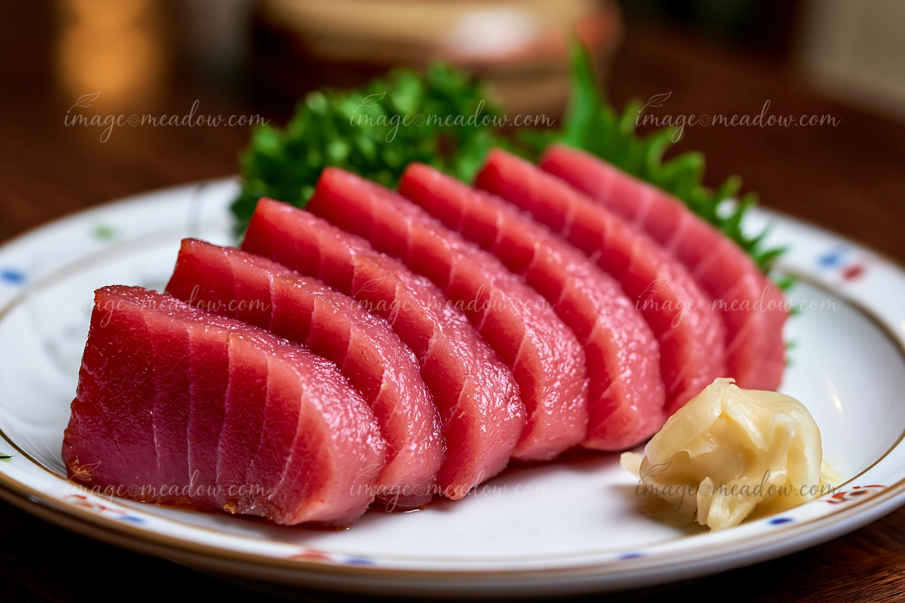 Slices of fresh tuna are arranged on a plate with green garnish and pickled ginger.