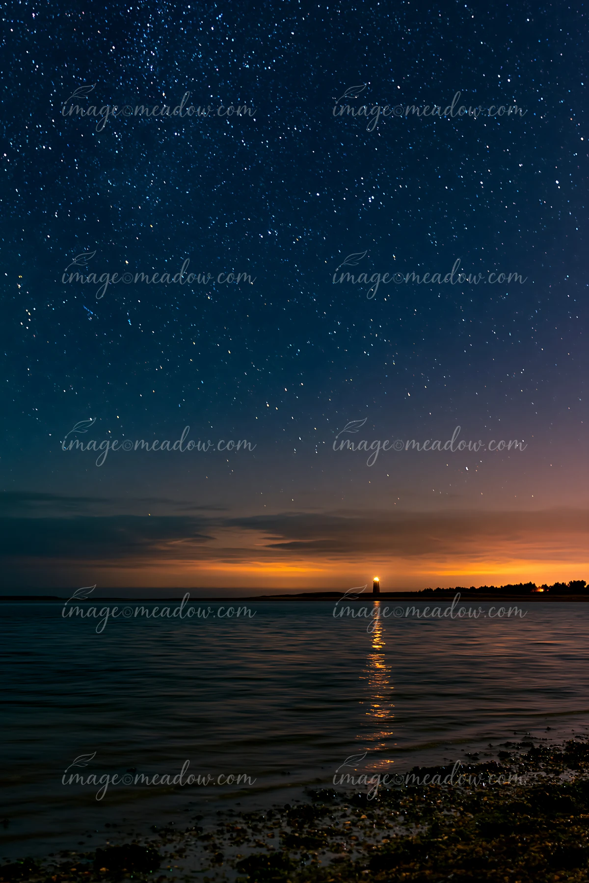 Stars fill the night sky over a calm ocean, with a lighthouse visible on the horizon reflecting light on the water.
