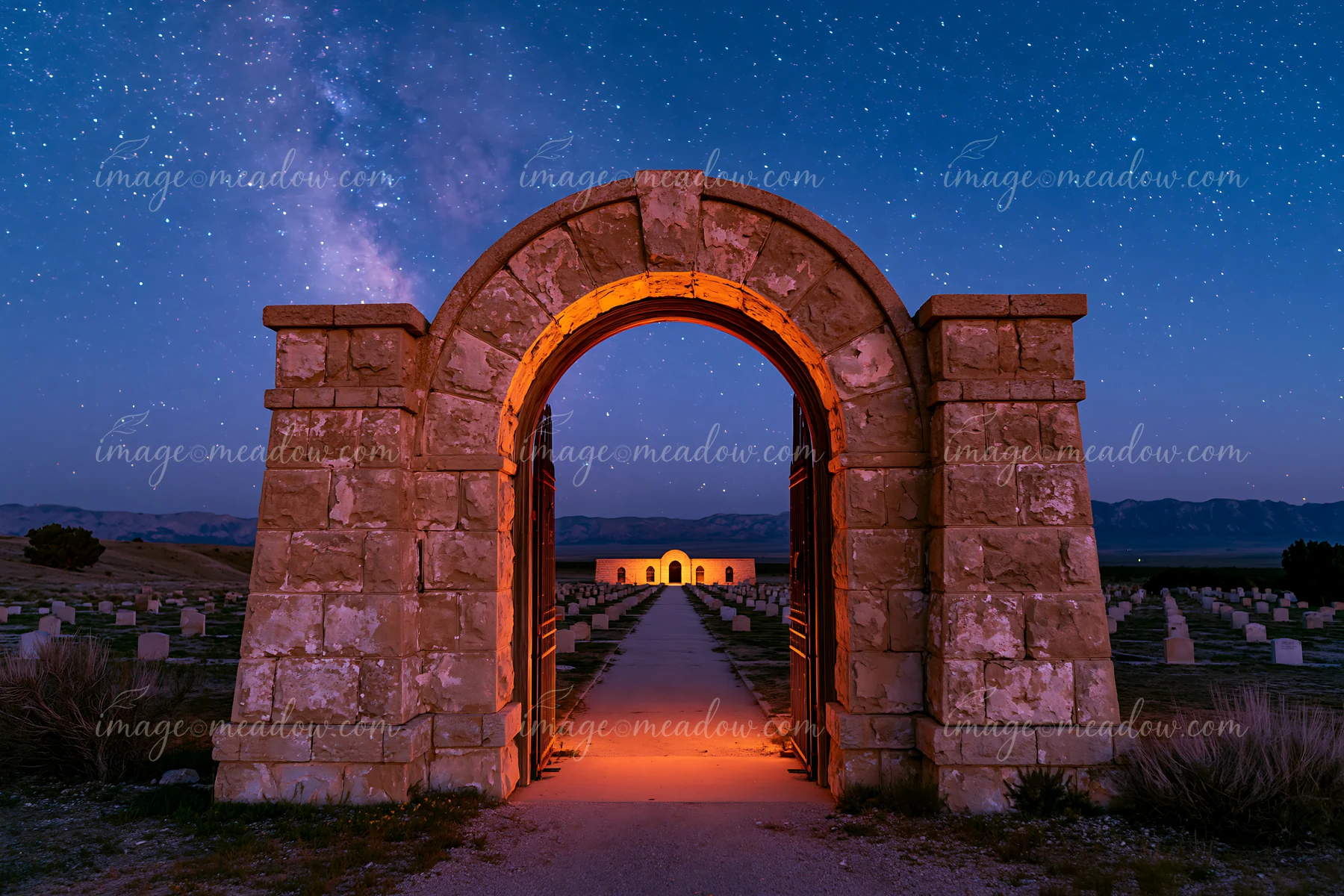 Stone archway opening onto a cemetery beneath a starry night sky, with mountains and rows of headstones beyond.