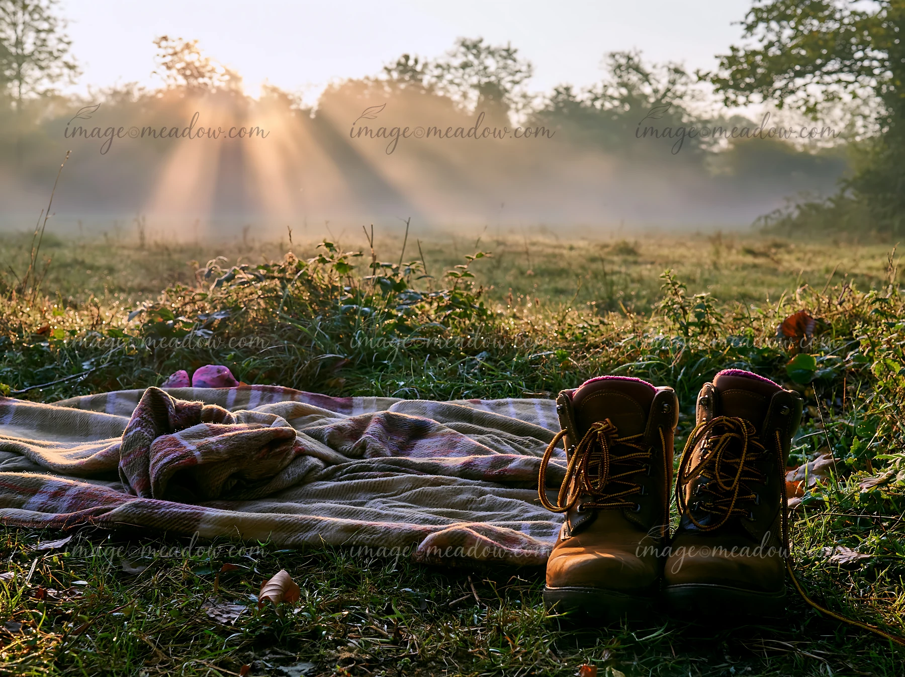 Sunbeams over a misty meadow highlight a blanket and a pair of boots.