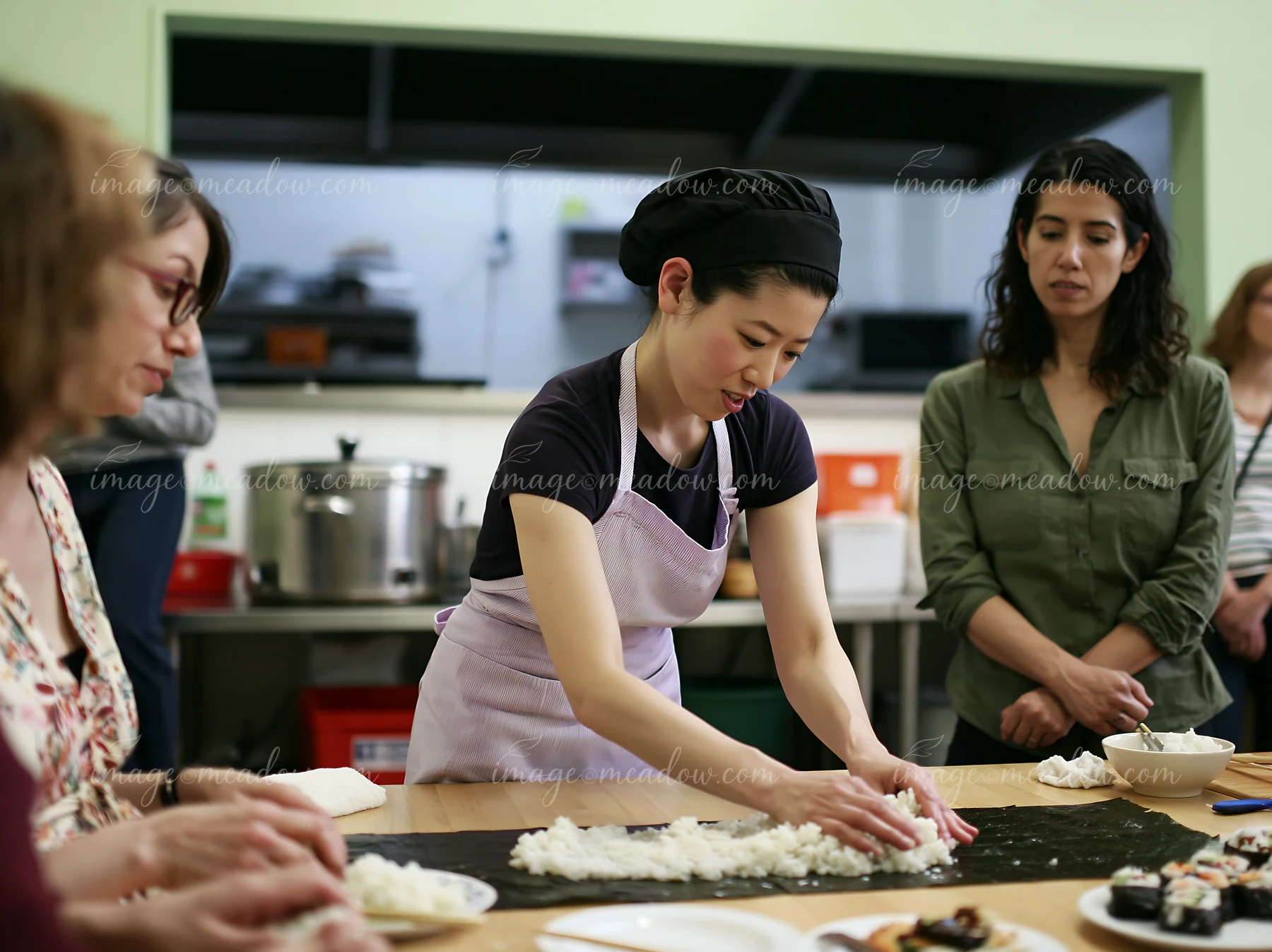 Sushi chef demonstrates rice preparation to adults during a hands-on class in a kitchen.